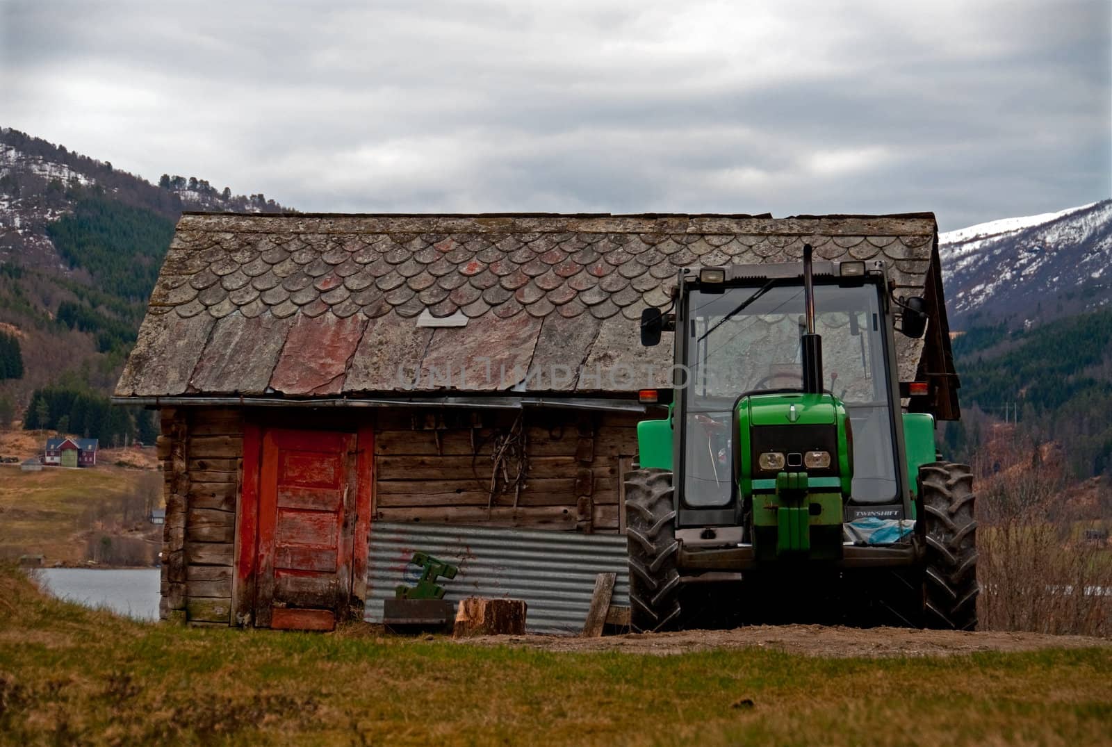 A green tractor standing in front of an old shed
