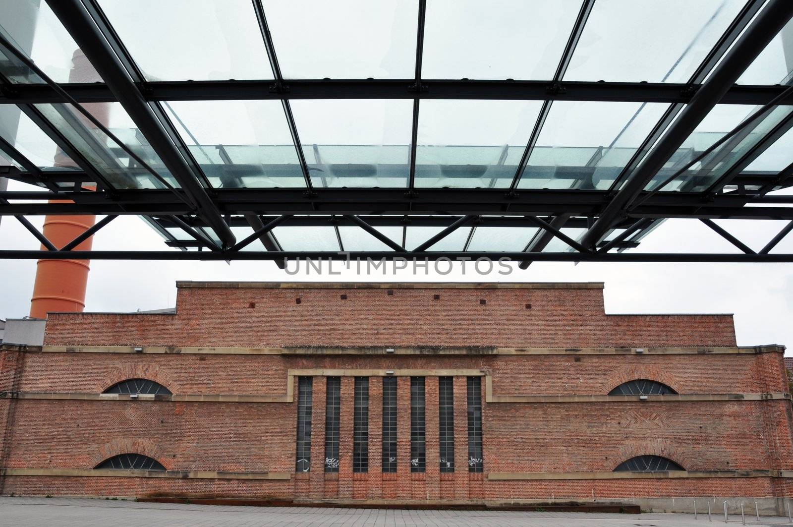 side wall of an old factory with chimney viewed from under a modern glass roof
