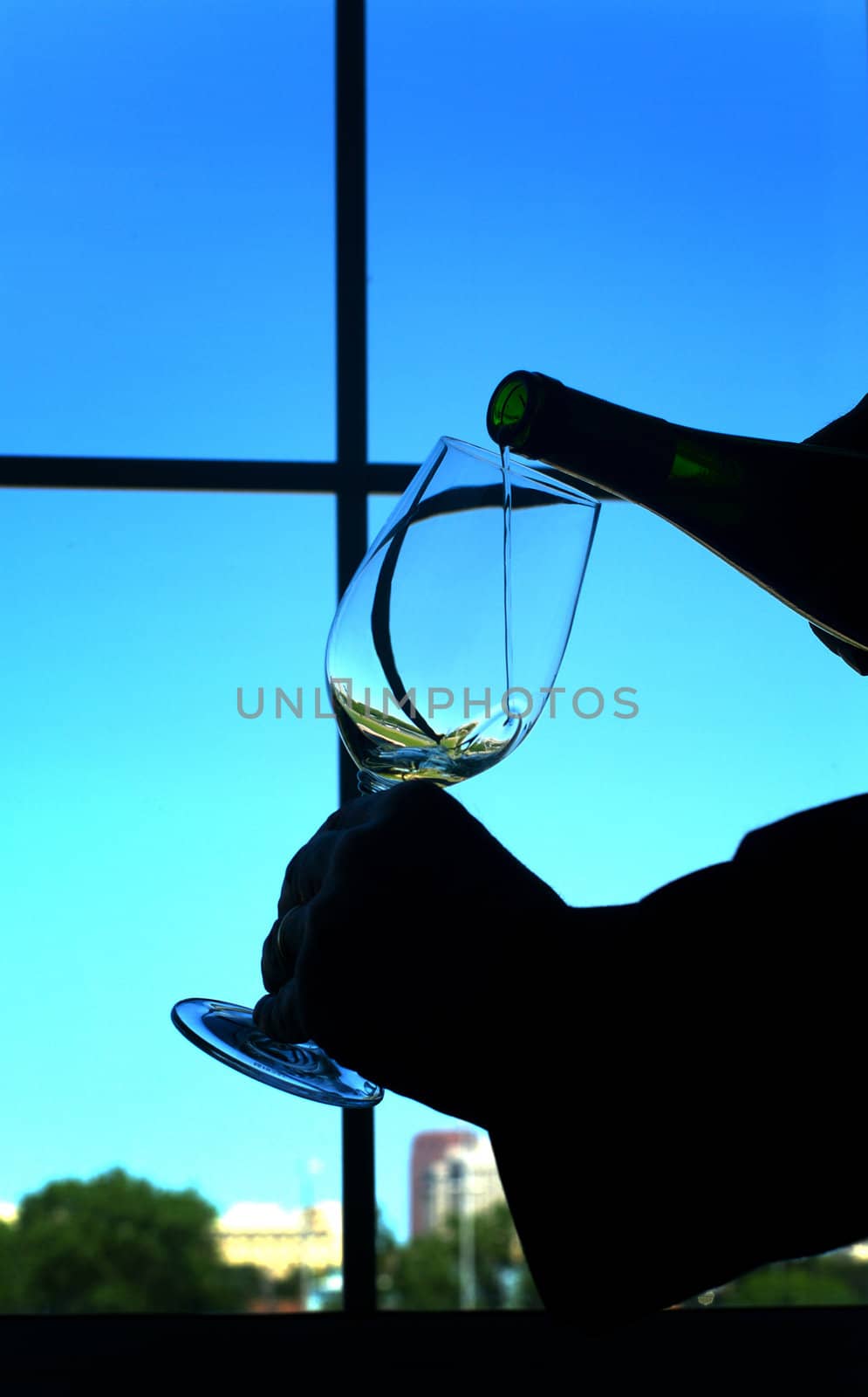 Silhouette of wine being poured into a glass against window and blue sky
