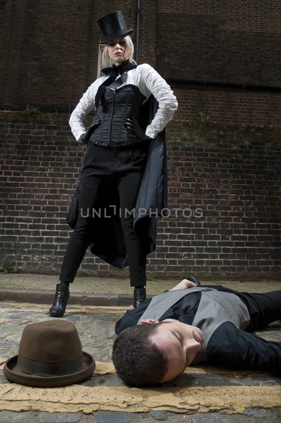 Woman dressed as Jack the Ripper on top of man lying on the ground.
