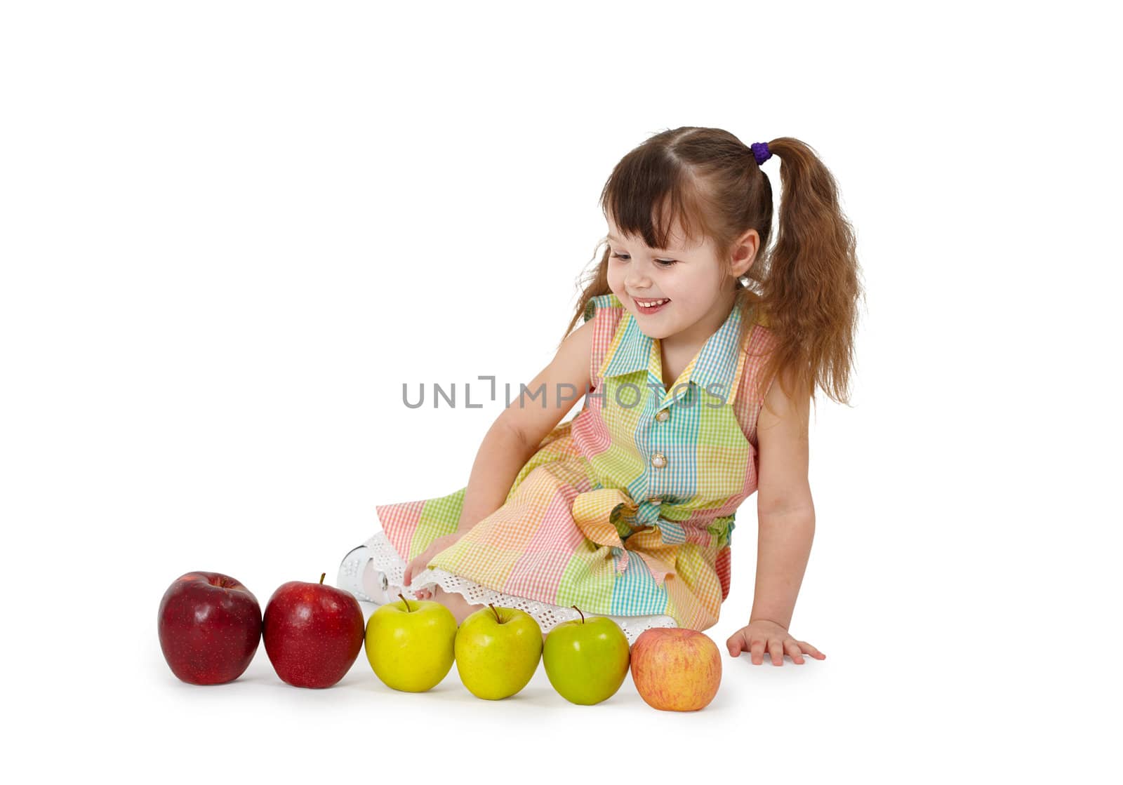The little girl sits on a white background with apples