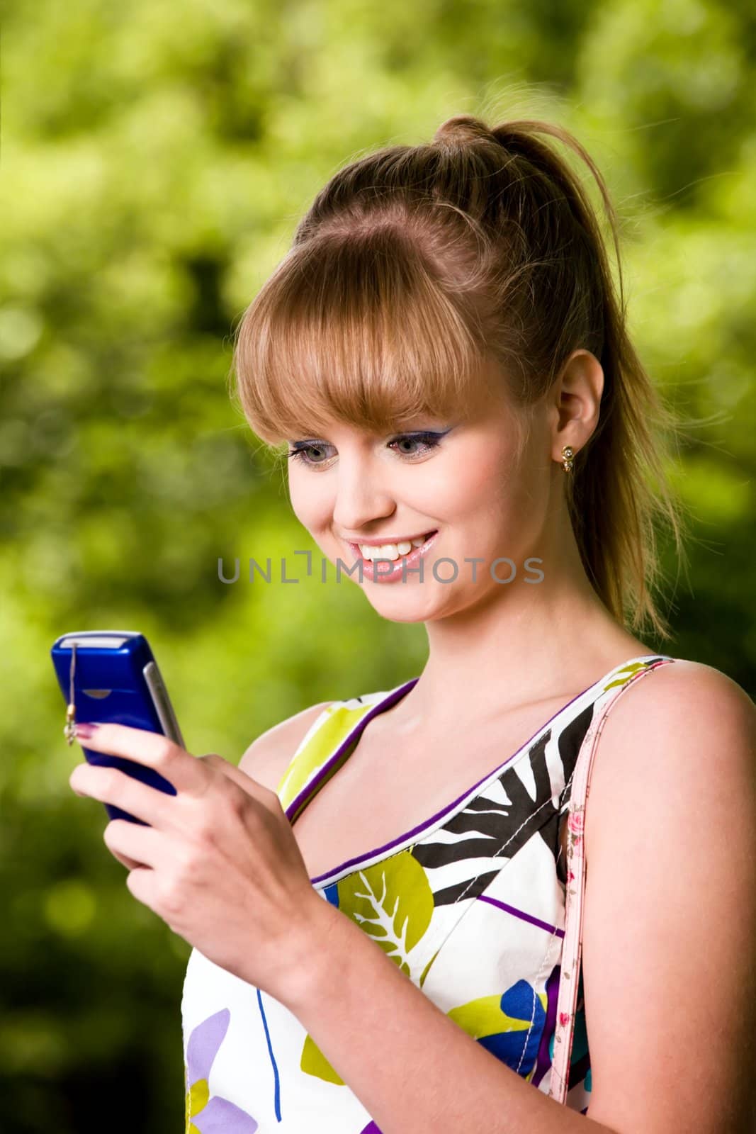 Smiling blond young woman with mobile phone outdoors