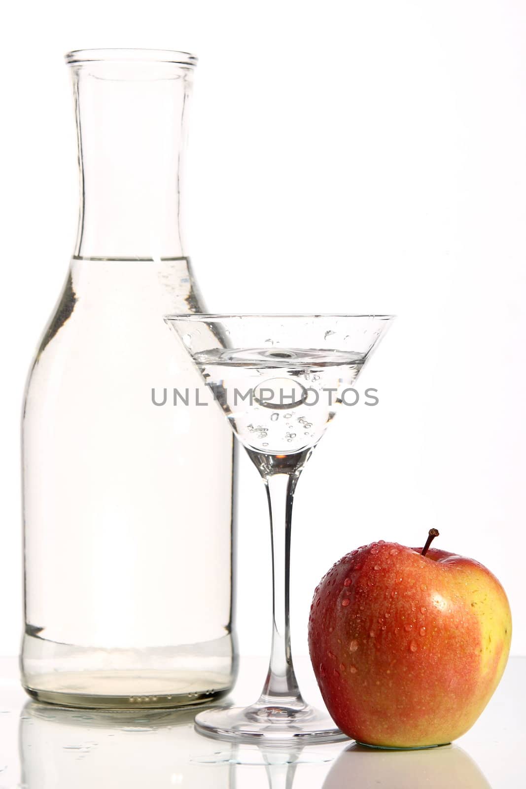 Bottle with transparent water, a glass and apples on a white background