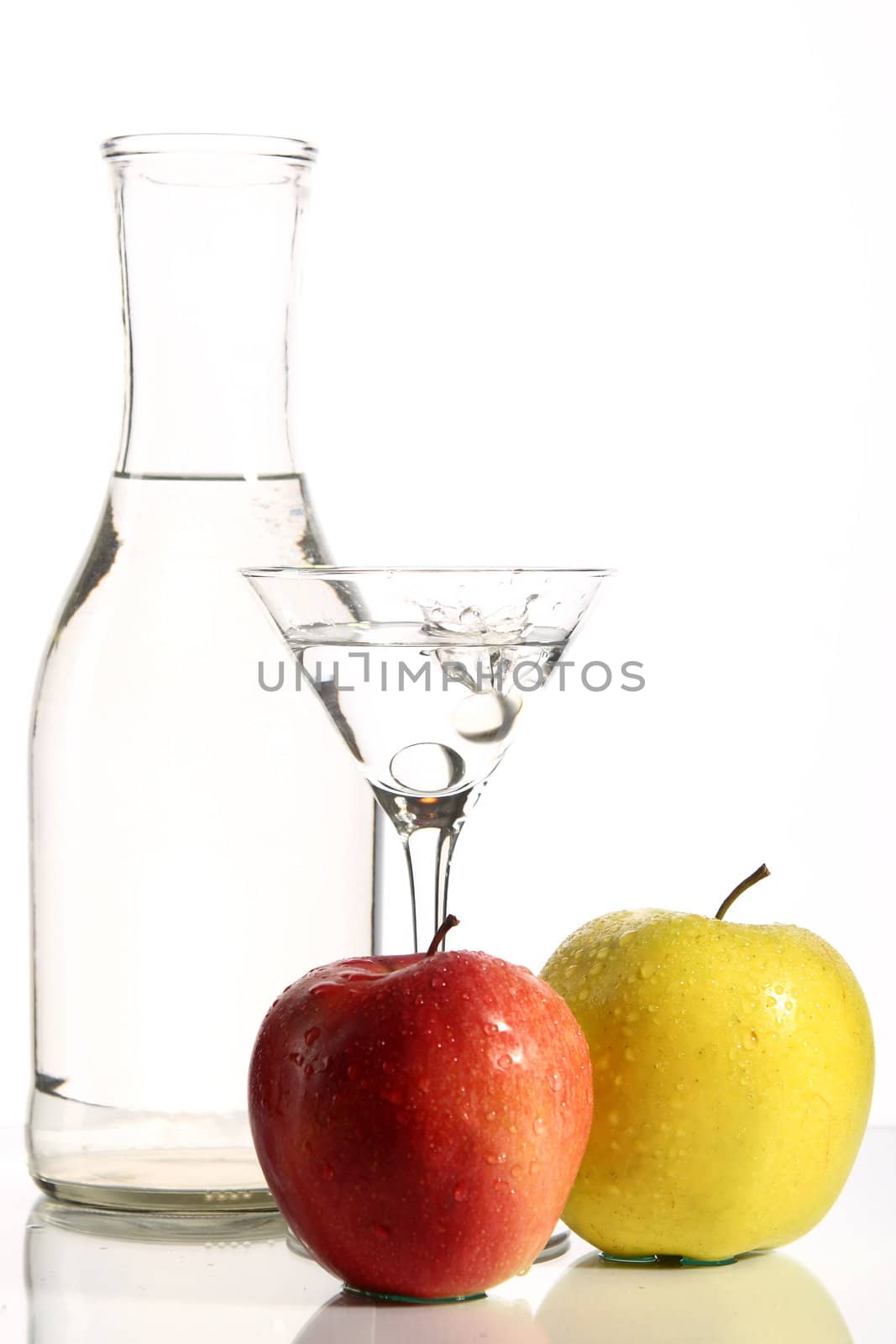 Bottle with transparent water, a glass and apples on a white background