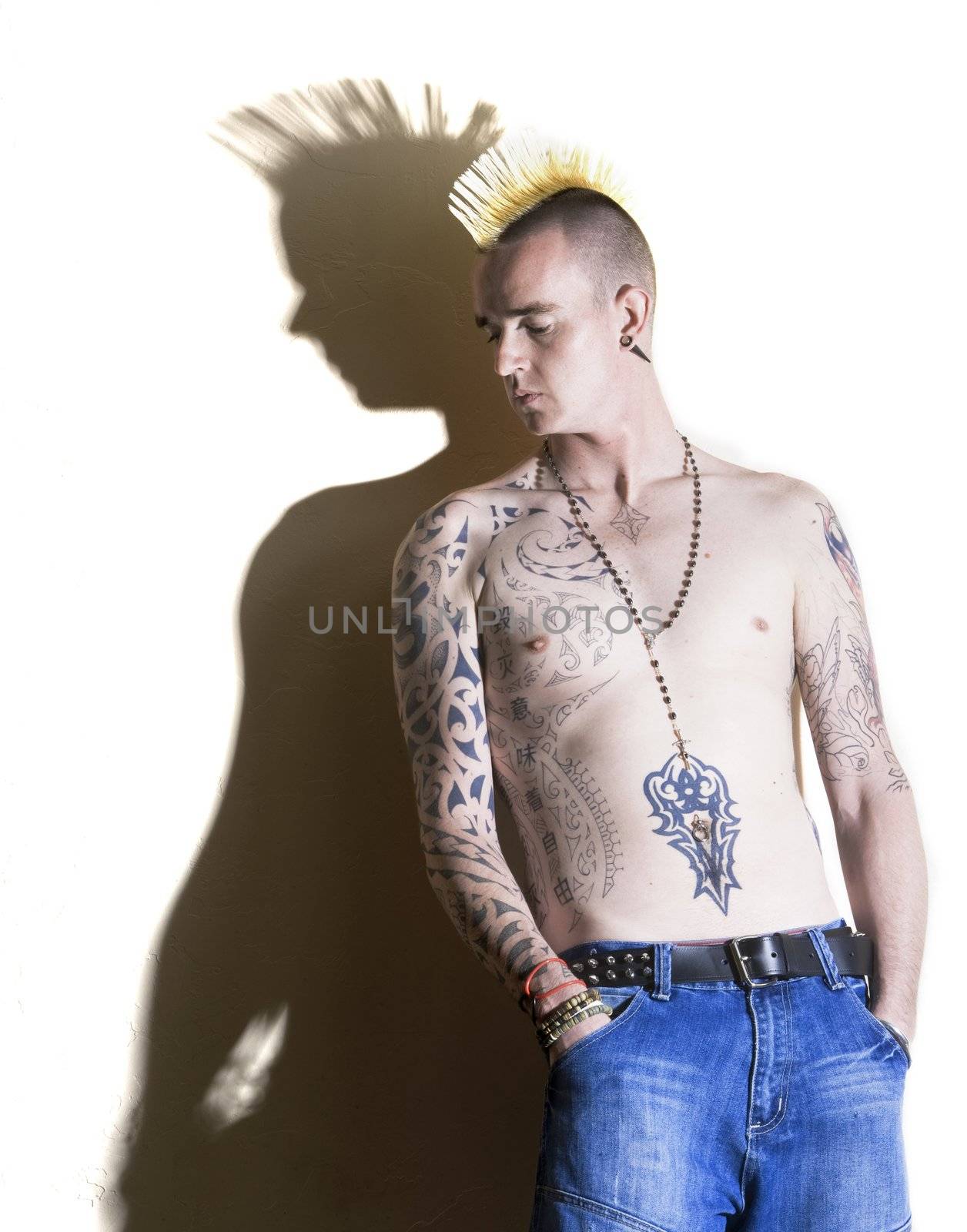 Punk with tattoos leaning against a white wall