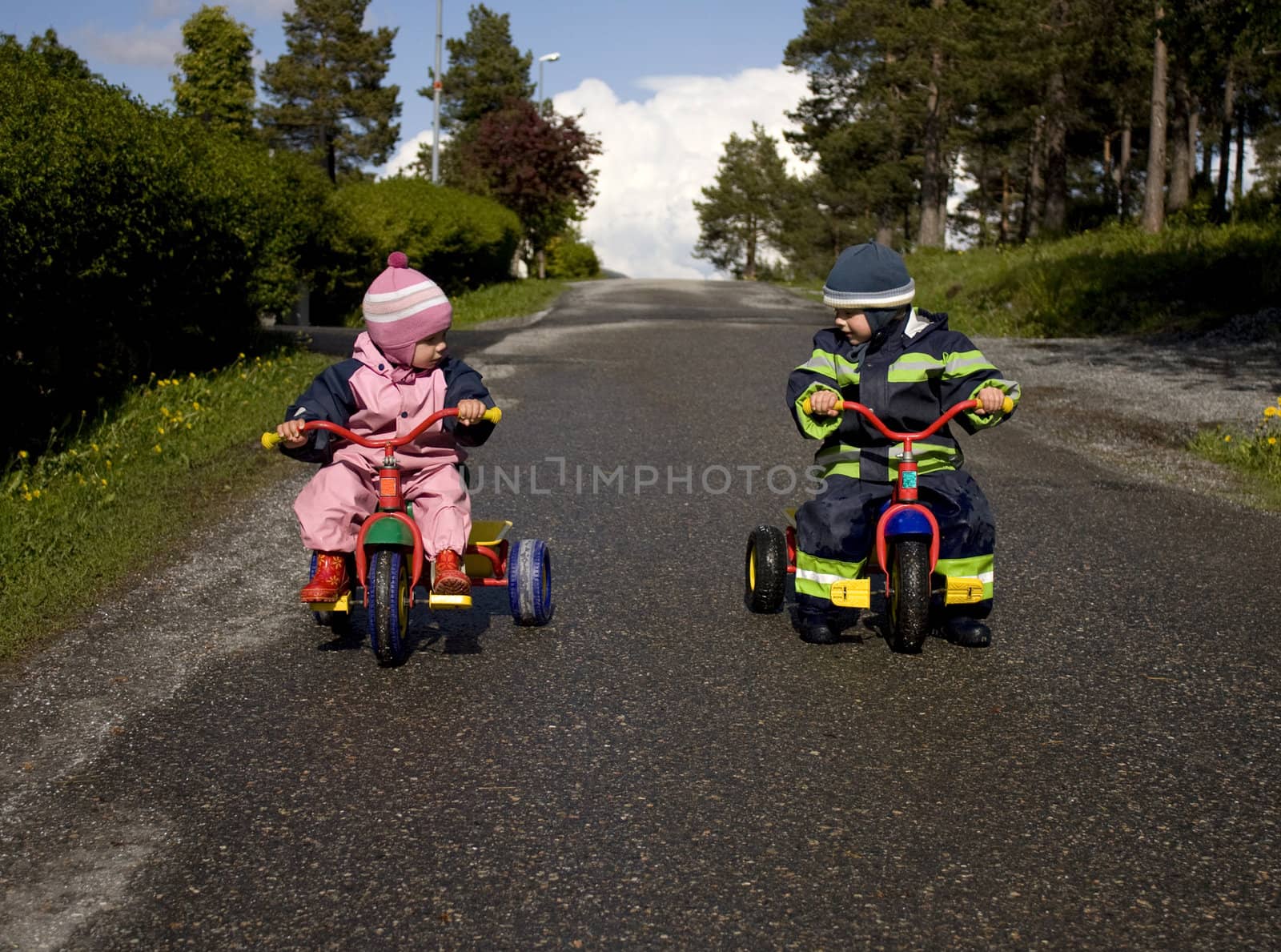 Brother and sister ready to race down a hill om tricycles
