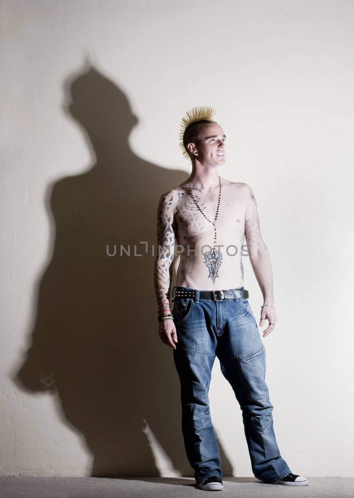 Punk with tattoos leaning against a white wall