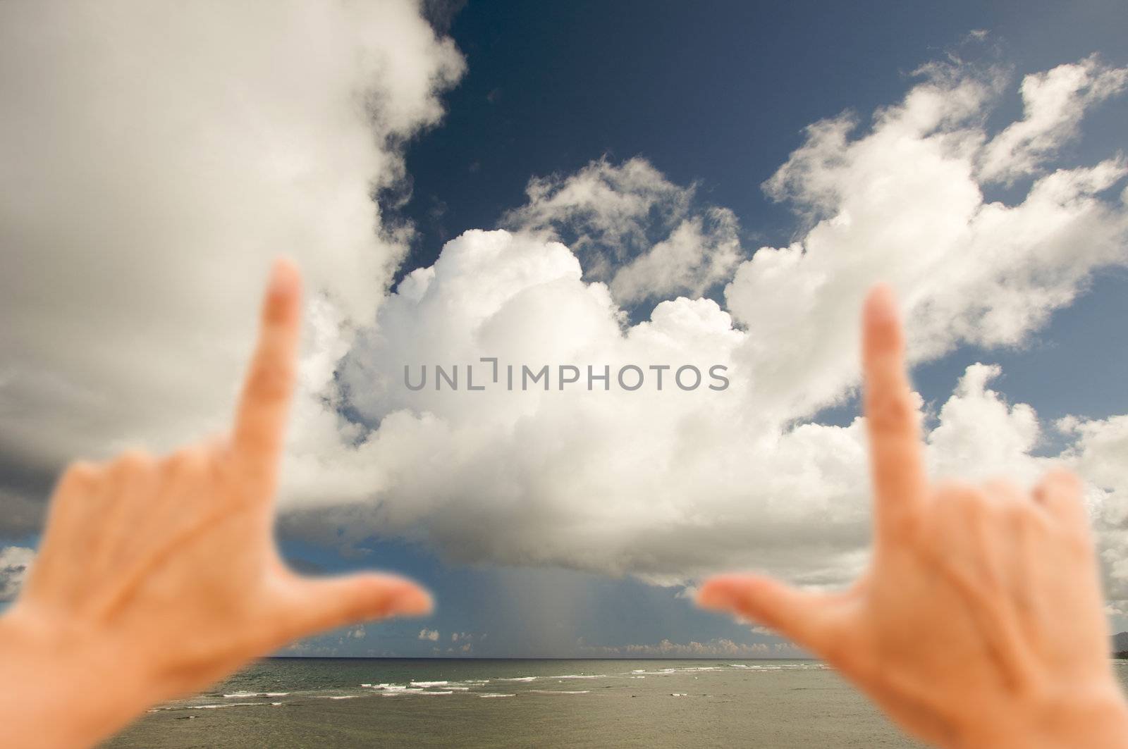Hands Framing Dramatic Clouds over Tropical Shoreline on Kauai, Hawaii