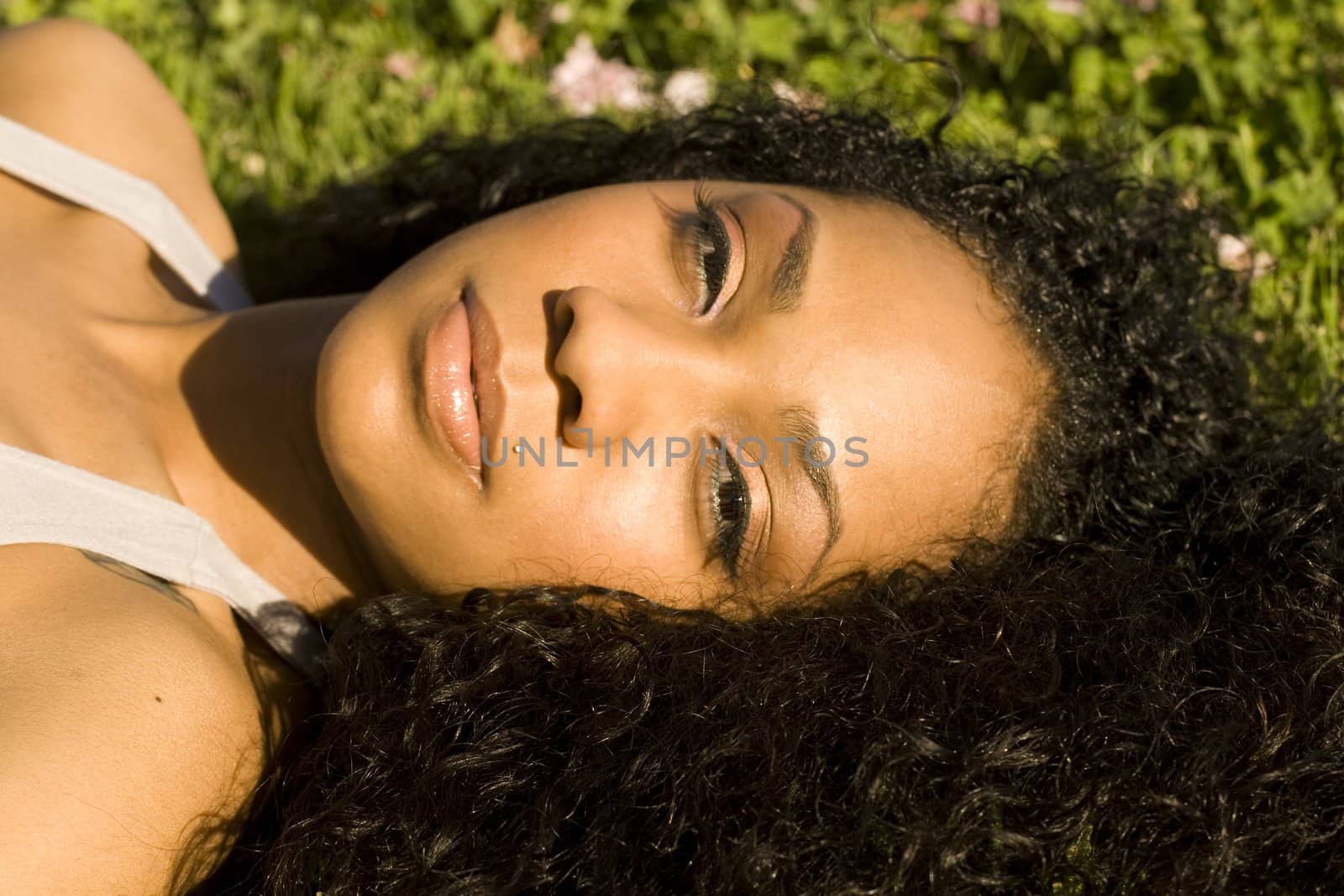Portrait of an attractive young black girl laying in green grass with flowers