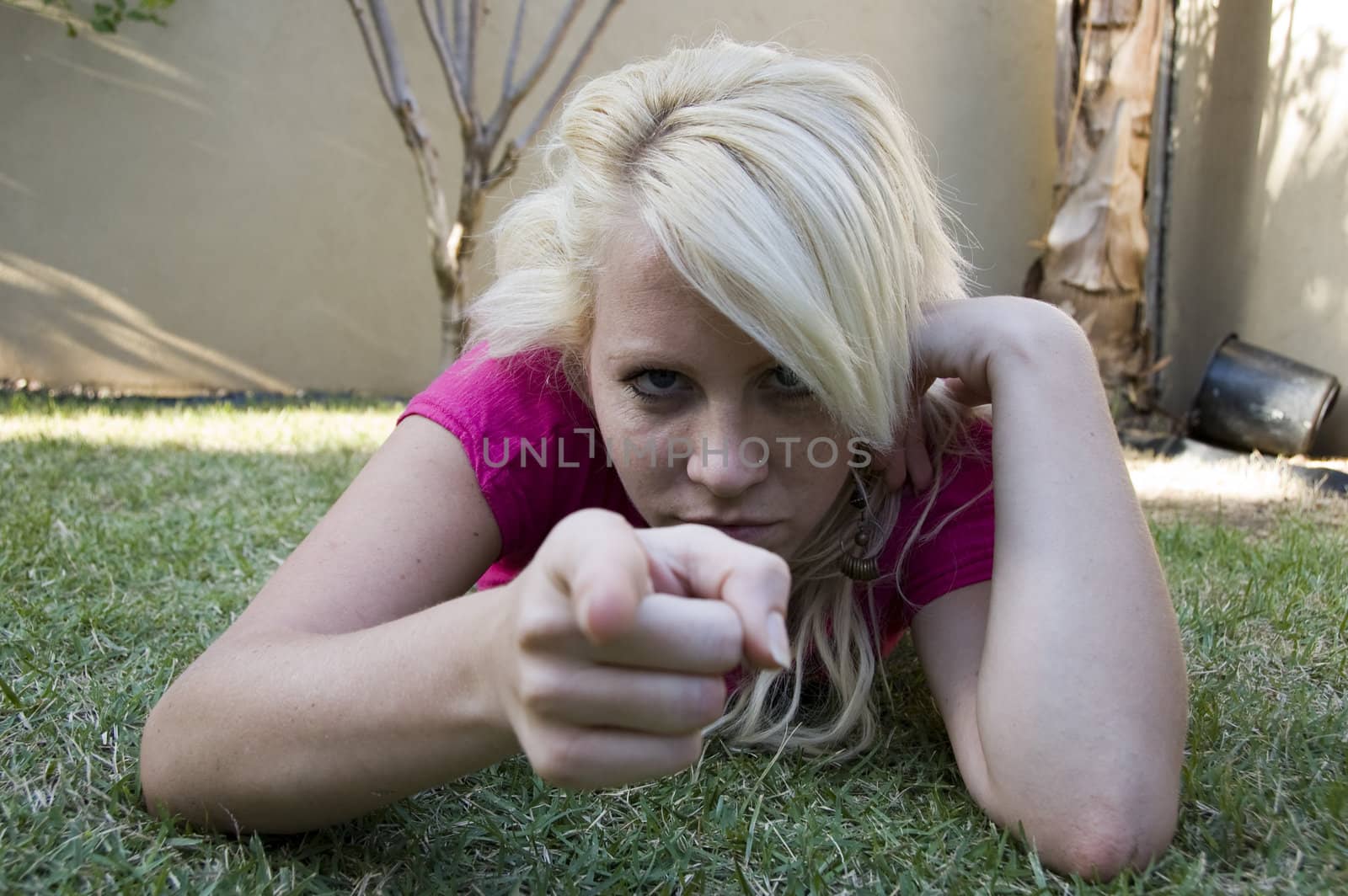 caucasian woman lying on grass pointing towards camera