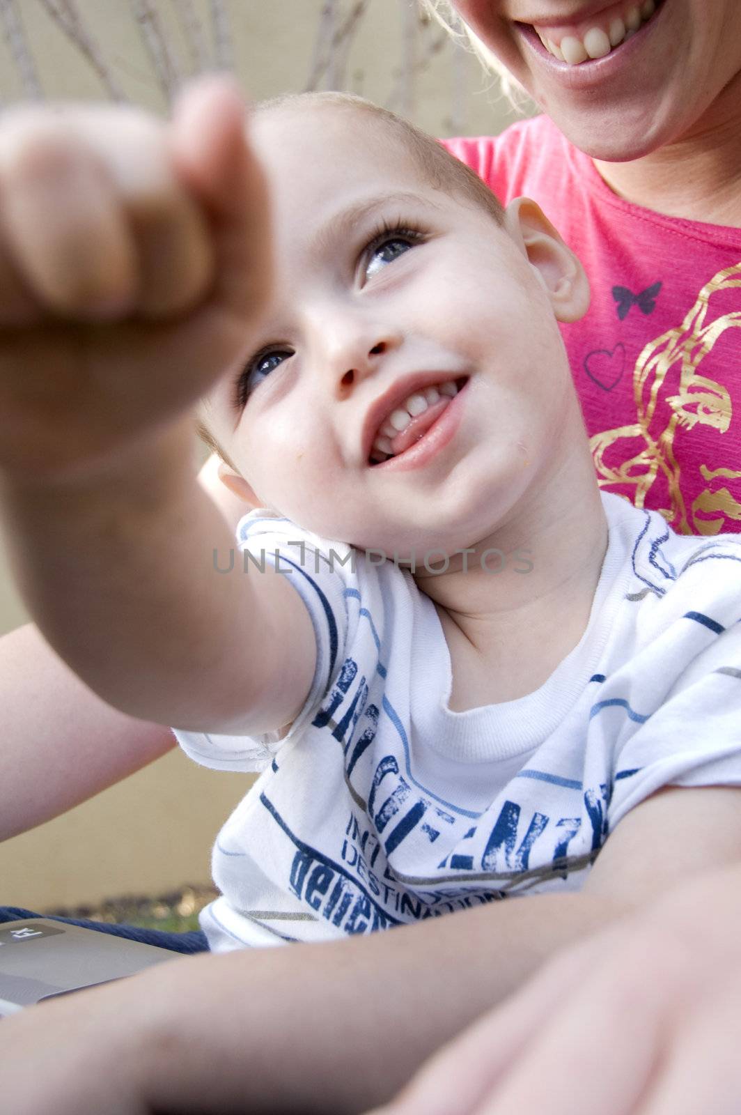 adorable young kid sitting with his mother pointing towards camera