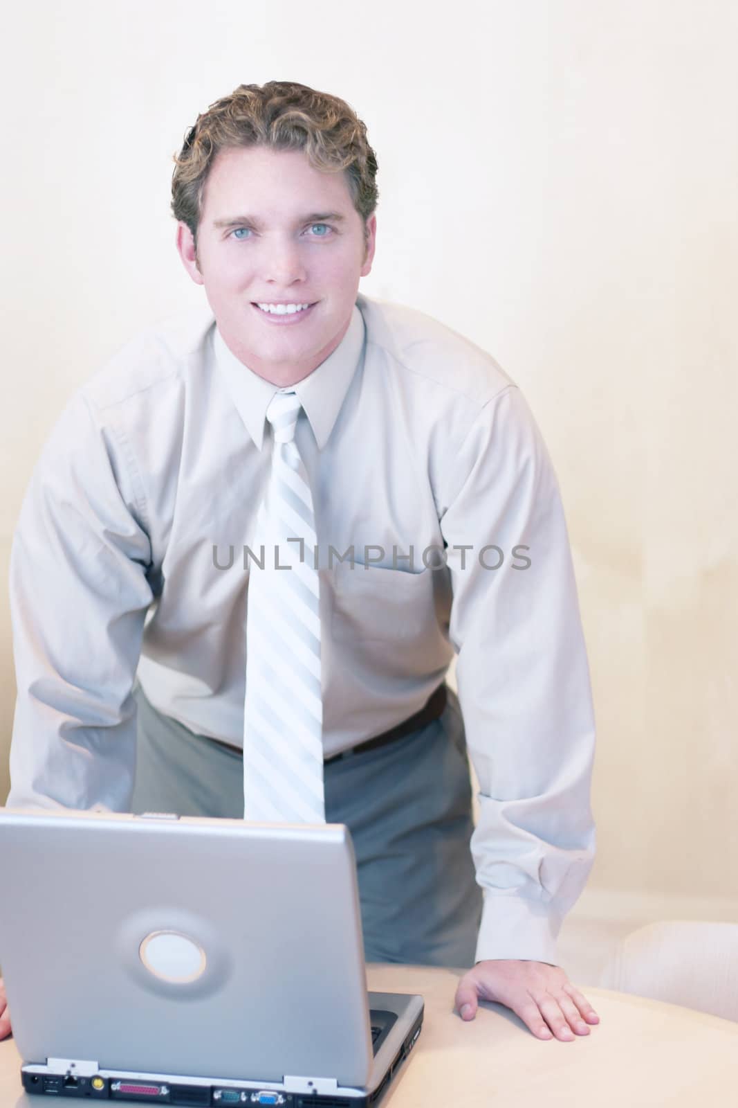Businessman smiling as he works on his laptop and stands over his desk wearing business casual clothes and a tie