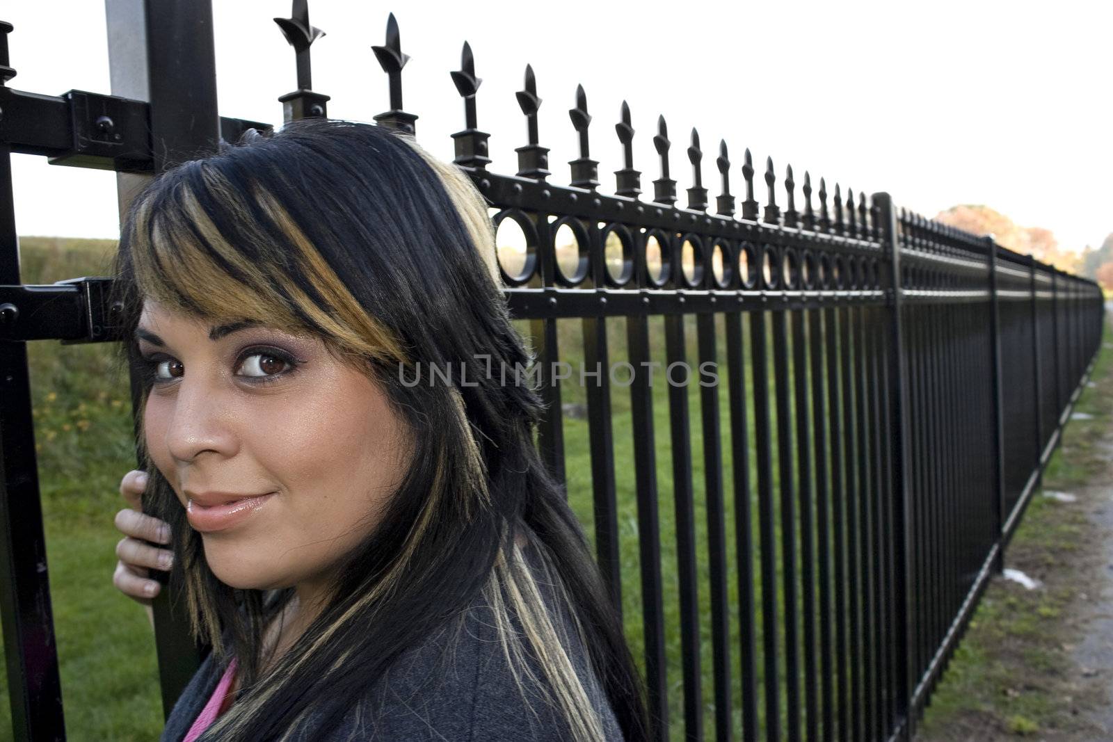 A young girl with highlighted hair posing by a fence on a nice autumn afternoon.