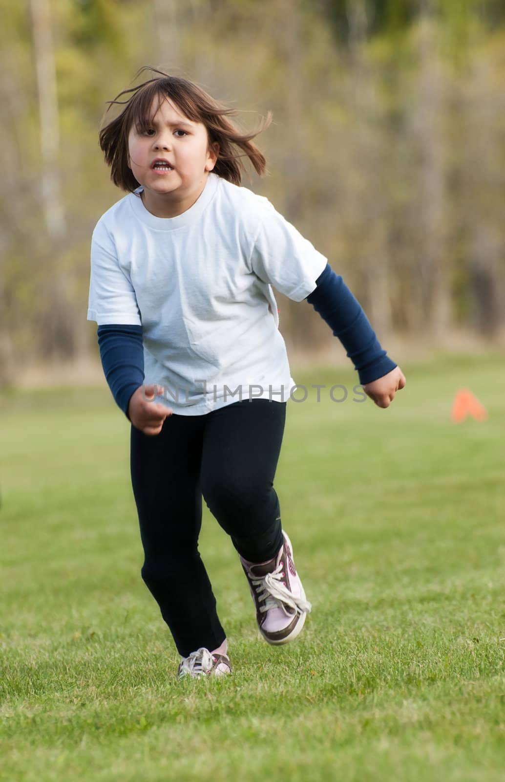 A young girl is running fast towards the camera, outside on a sunny day.