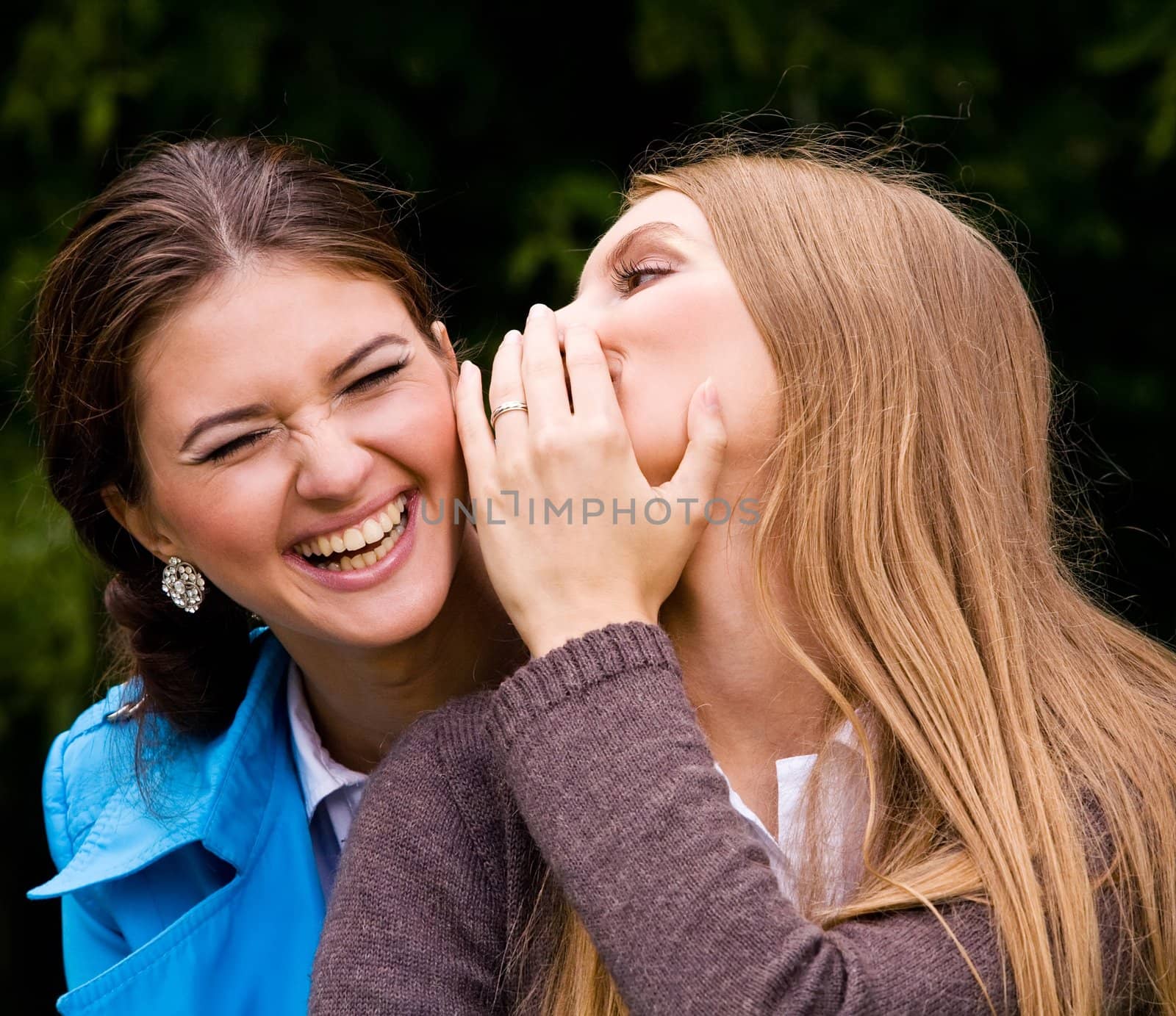 Two inseparable cheerful girlfriends laughing until one cries in summer park