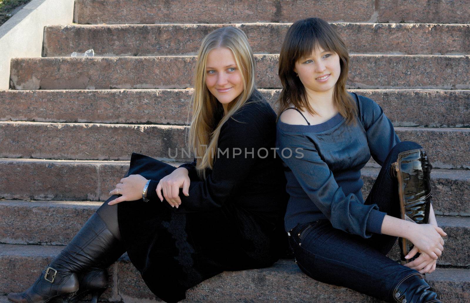 Two girlfriends sitting at ladder steps. Outdoor, park