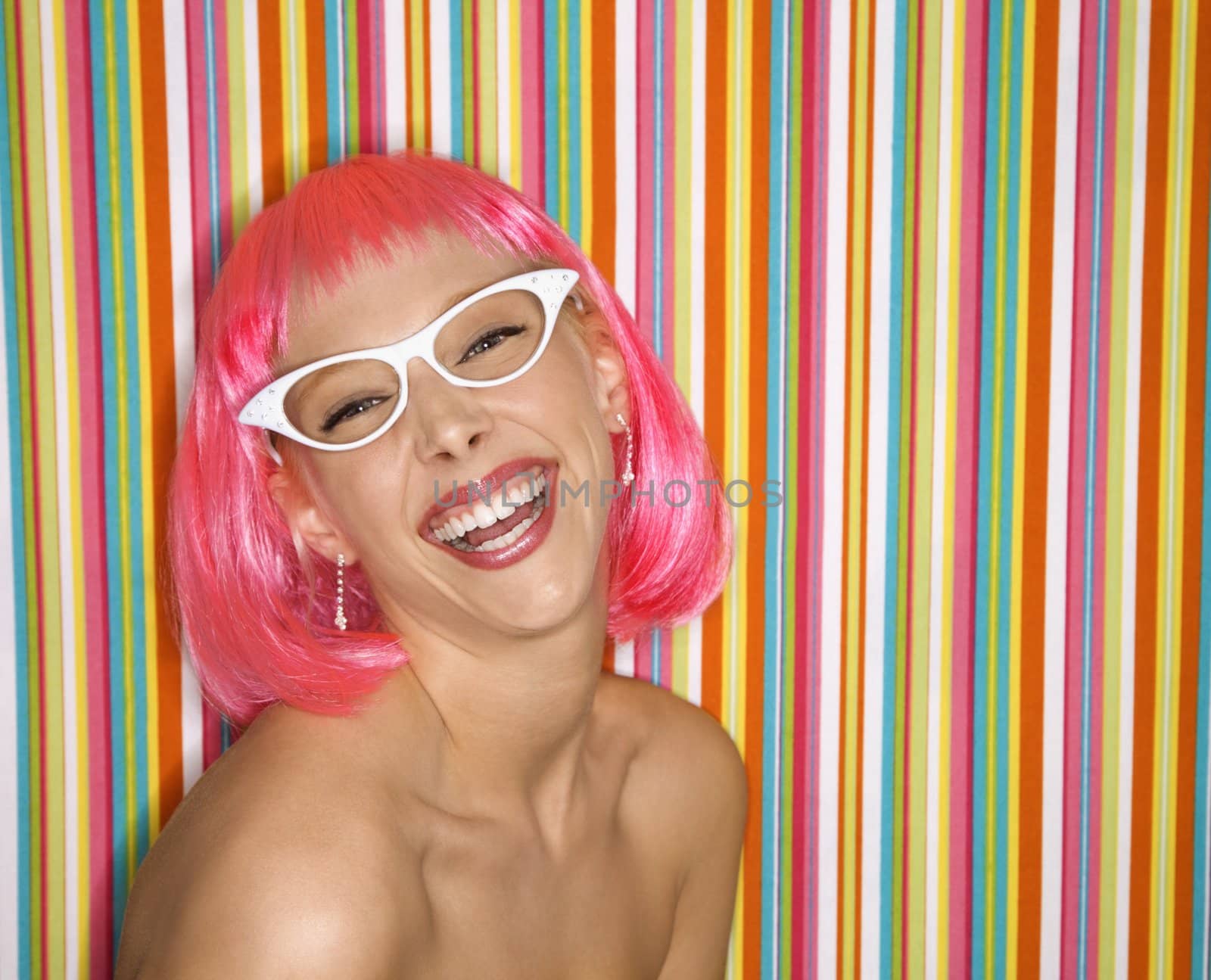 Portrait of attractive Caucasian young adult woman wearing pink wig against striped background making sassy expression looking at viewer.