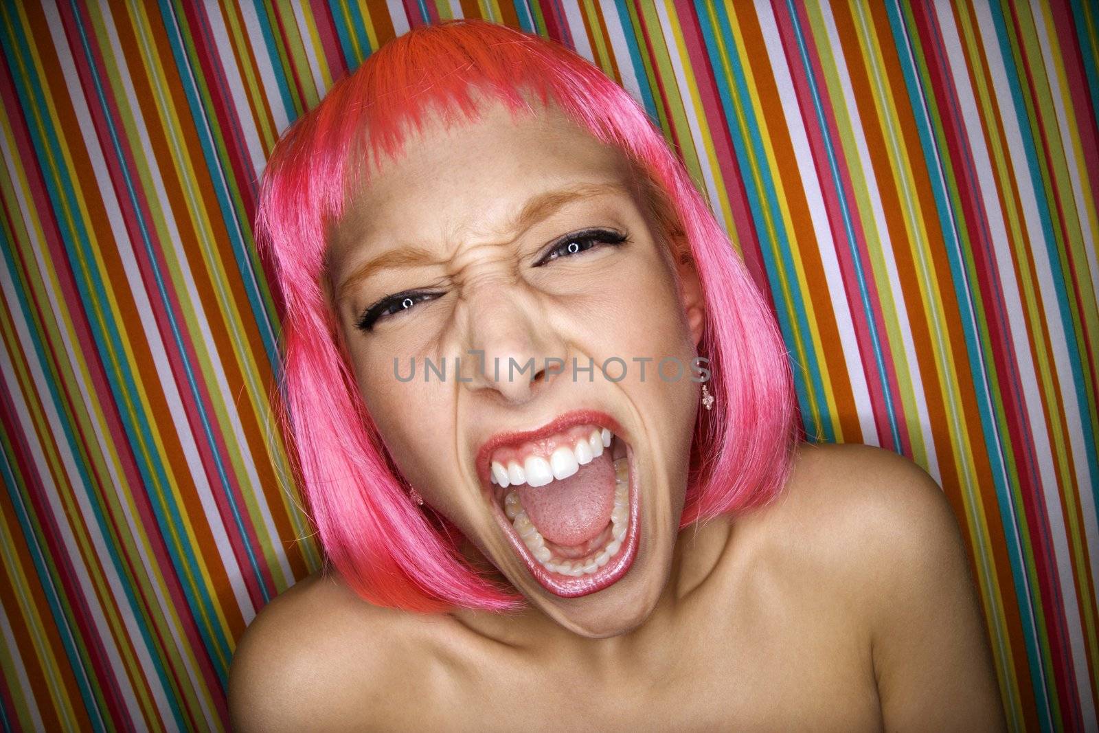 Portrait of attractive Caucasian young adult woman wearing pink wig against striped background making sassy expression at viewer.