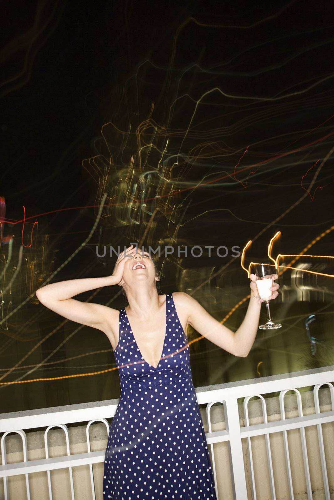 Pretty Caucasian young woman smiling and drinking at night with blurred lights.