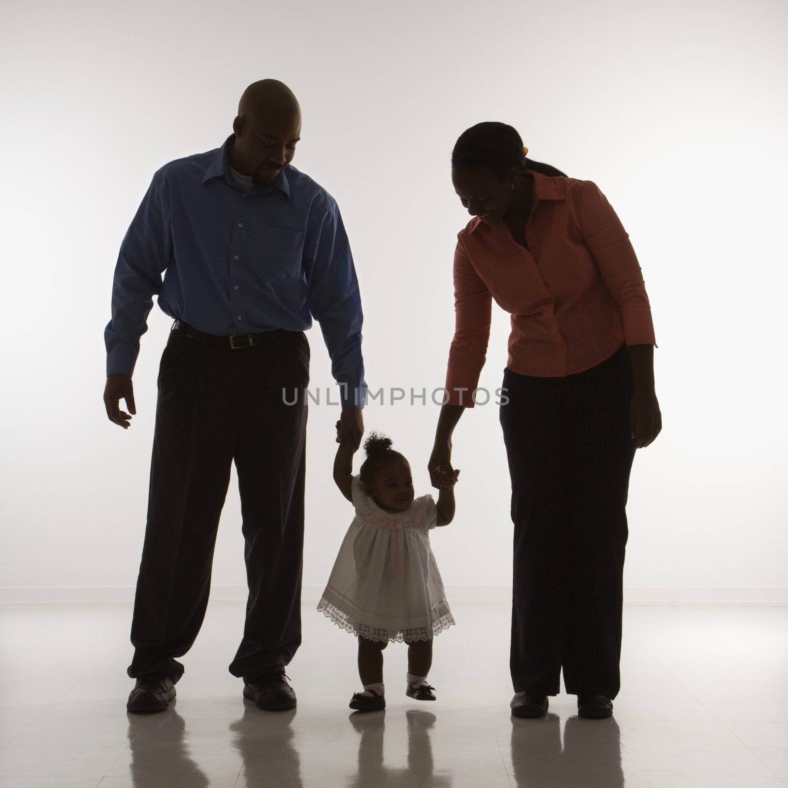 African American man and woman standing holding up infant girl by her hands against white background.