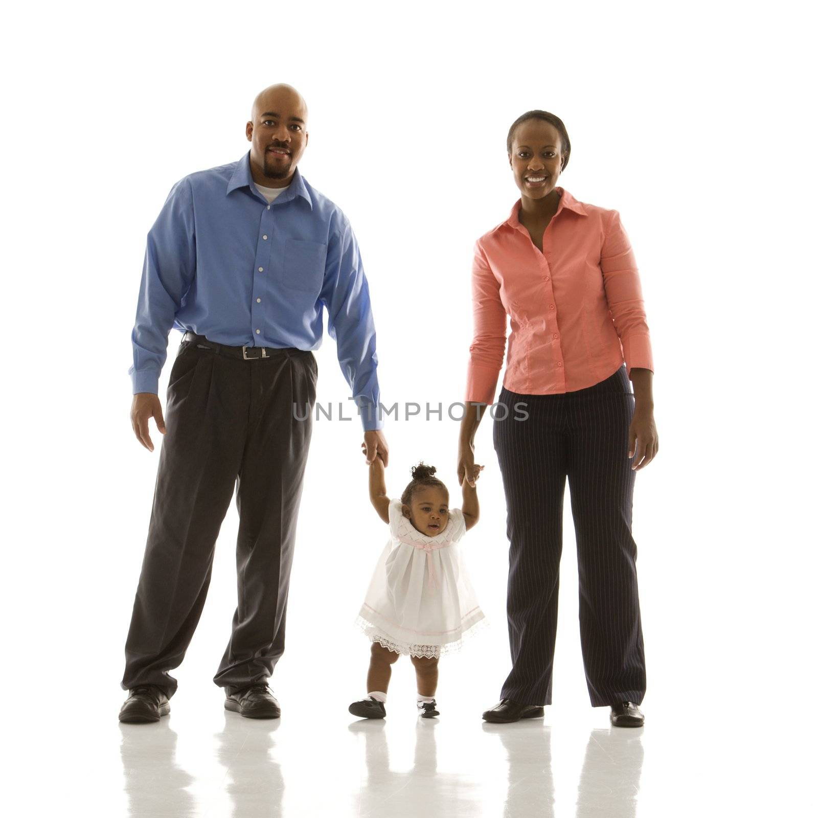 African American man and woman standing holding up infant girl by her hands against white background.