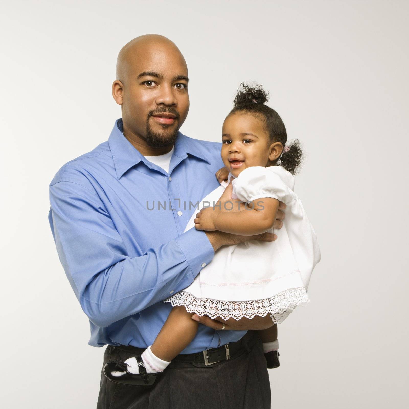 African American man holding infant girl standing against white background.