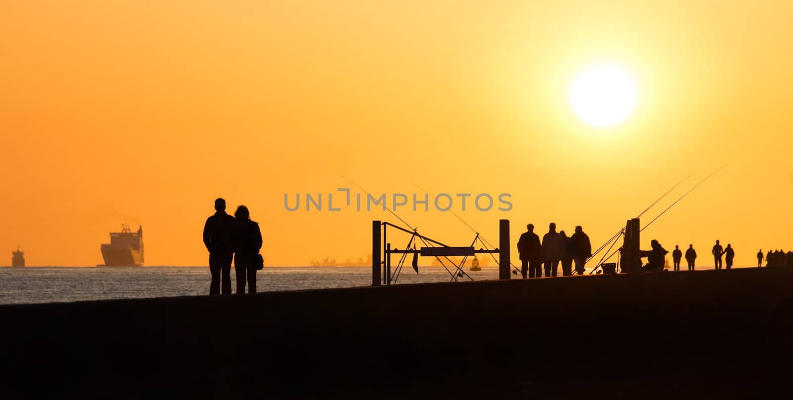 Pier with people fishing and walking - hazy and yellow sunset from volcanodust in the air