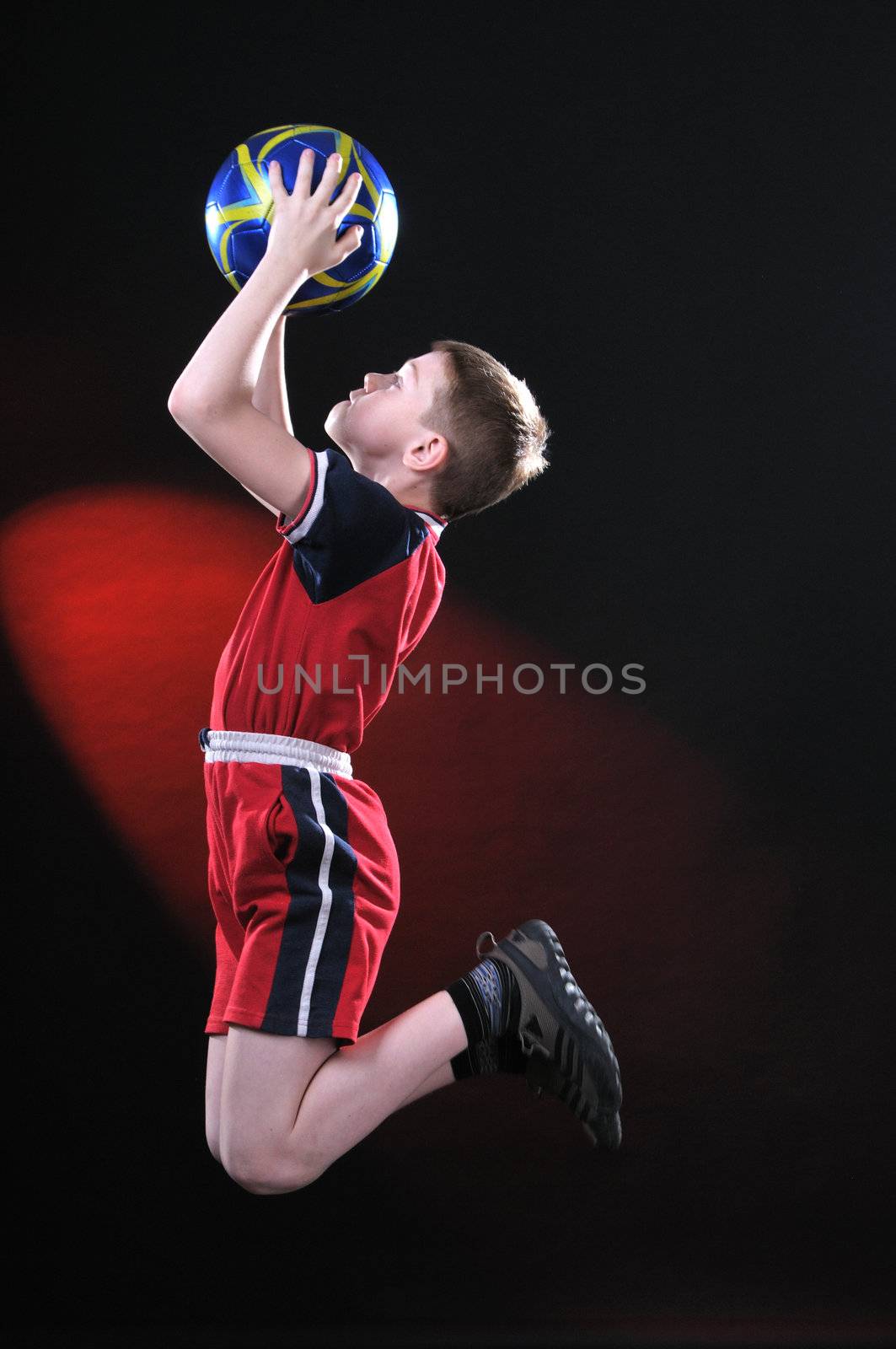 boy ten years in a jump on a dark background and catches a soccer ball