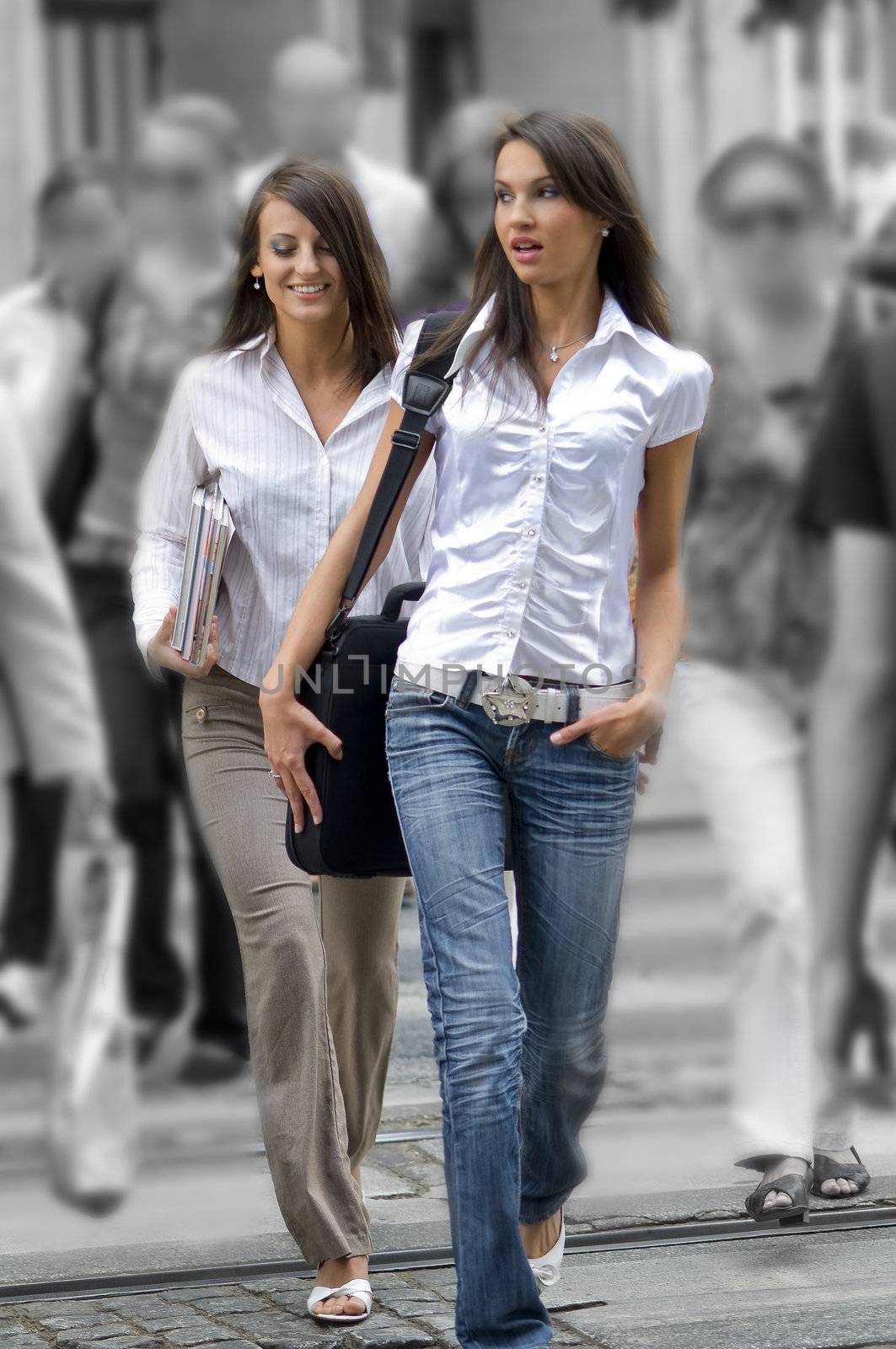 two young women between the crowd crossing the road in the center of town