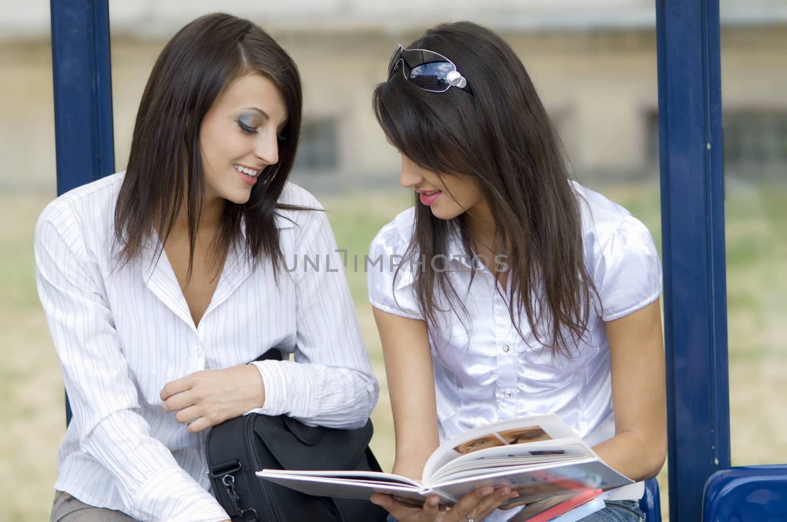 young women talking togheter about a make up book at the bus stop in the central town