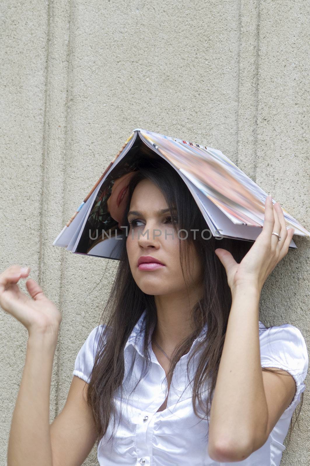 nice student girl sitting against a wall and using a book in an unusual way