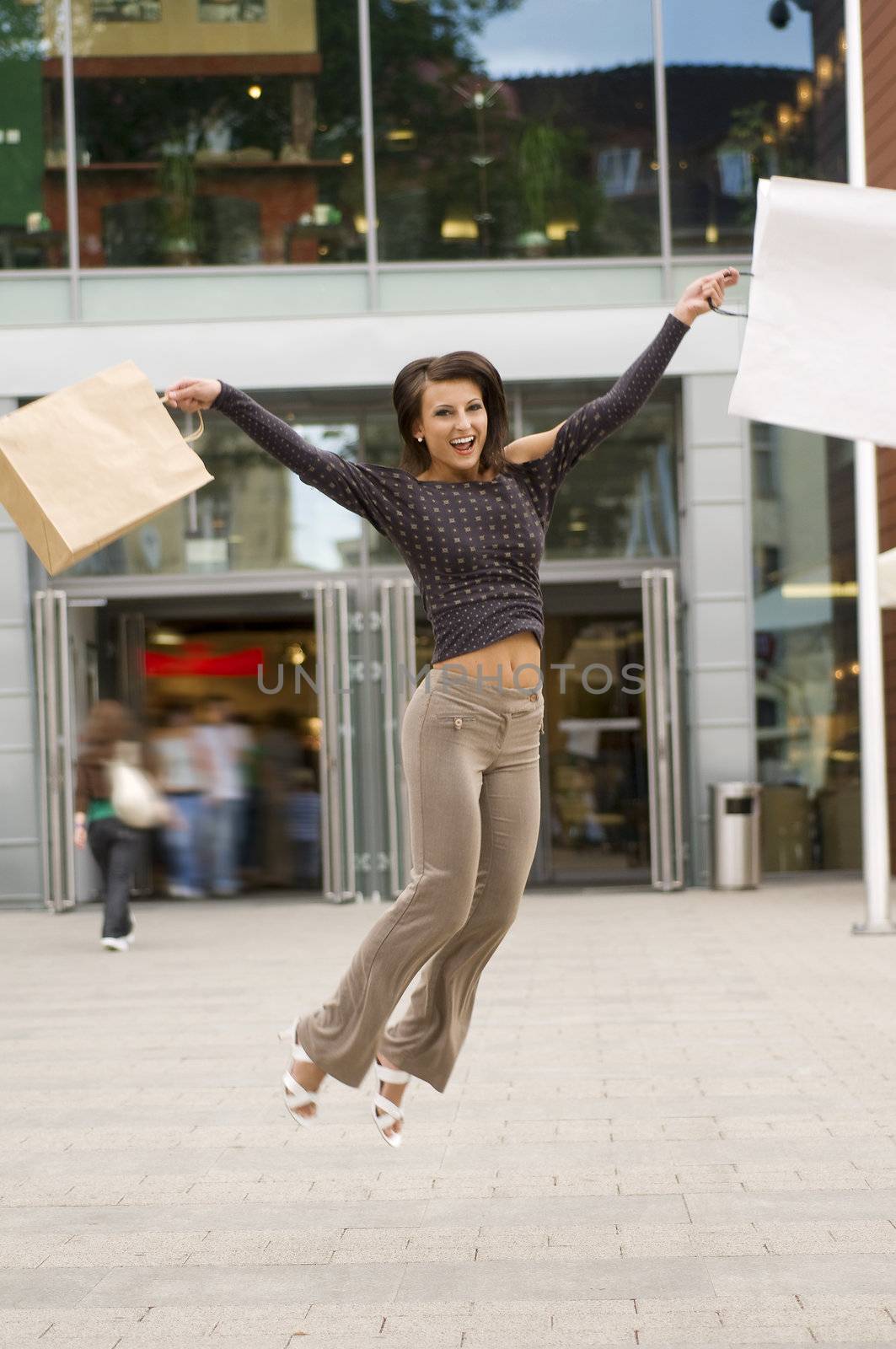 cute brunette jumping for joy in front of a commercial center after shopping