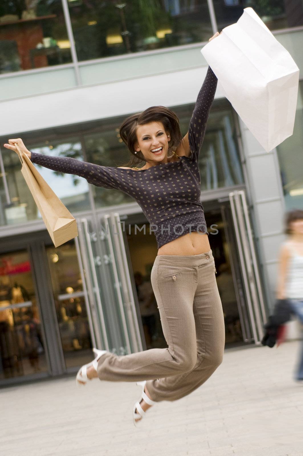 cute brunette jumping for joy in front of a commercial center after some purchases