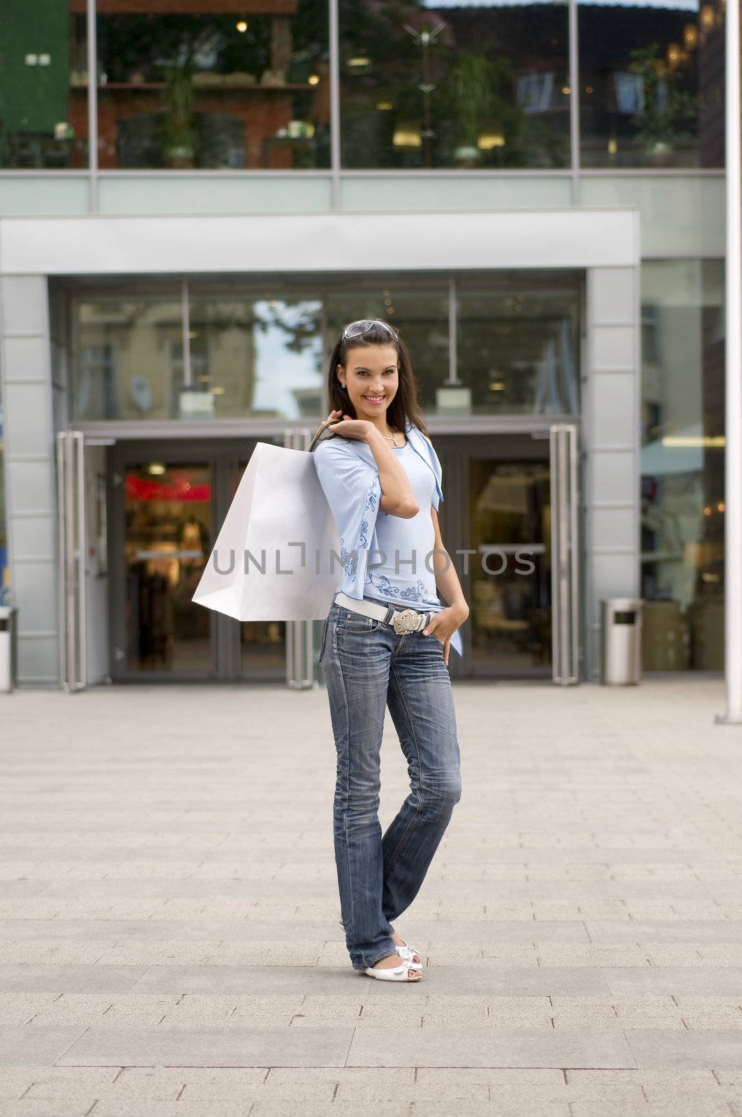 cute brunette standing in front of a commercial center with bags on her shoulder