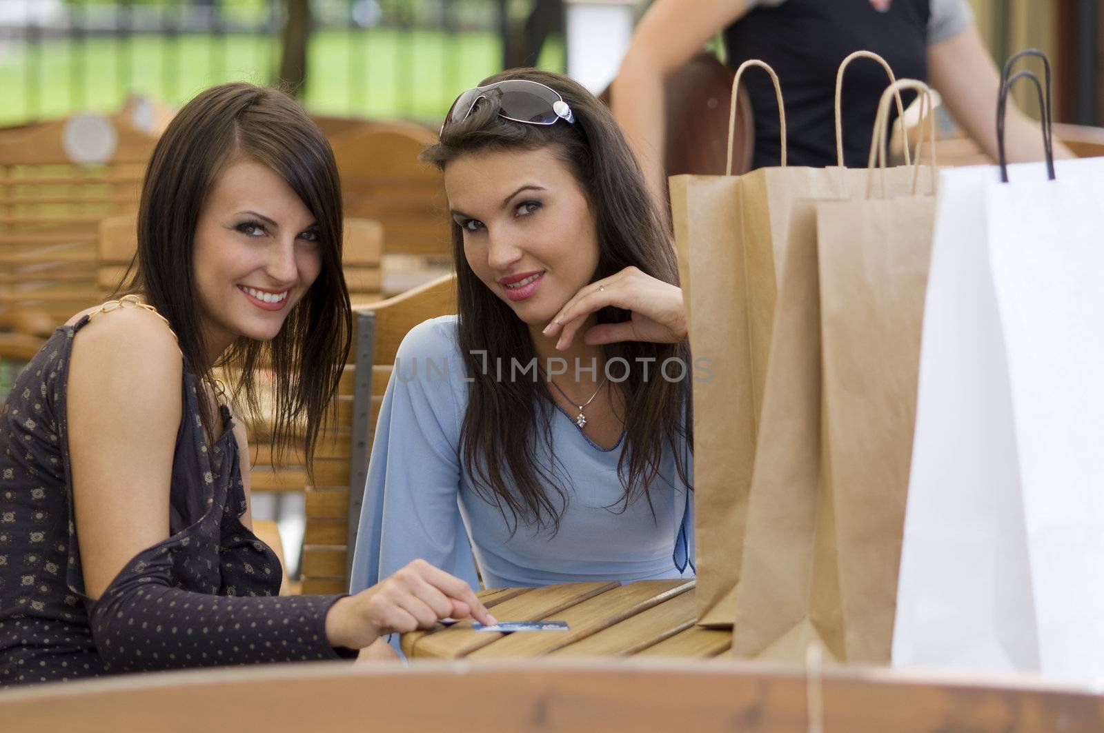 two pretty girls sitting outdoor with shopping bags and credit cards