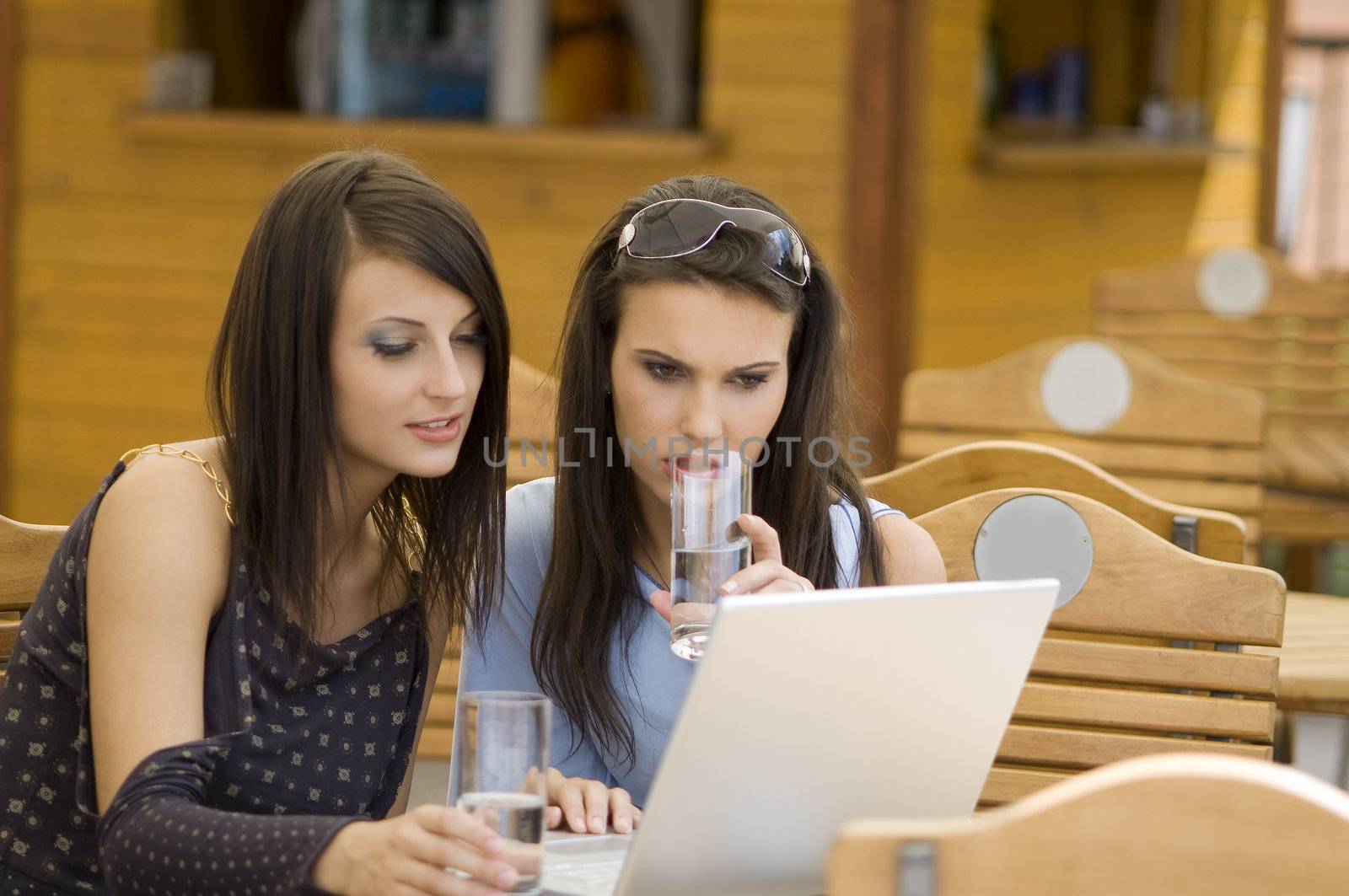 two young woman sitting in a outdoor pub looking at the computer and drinking