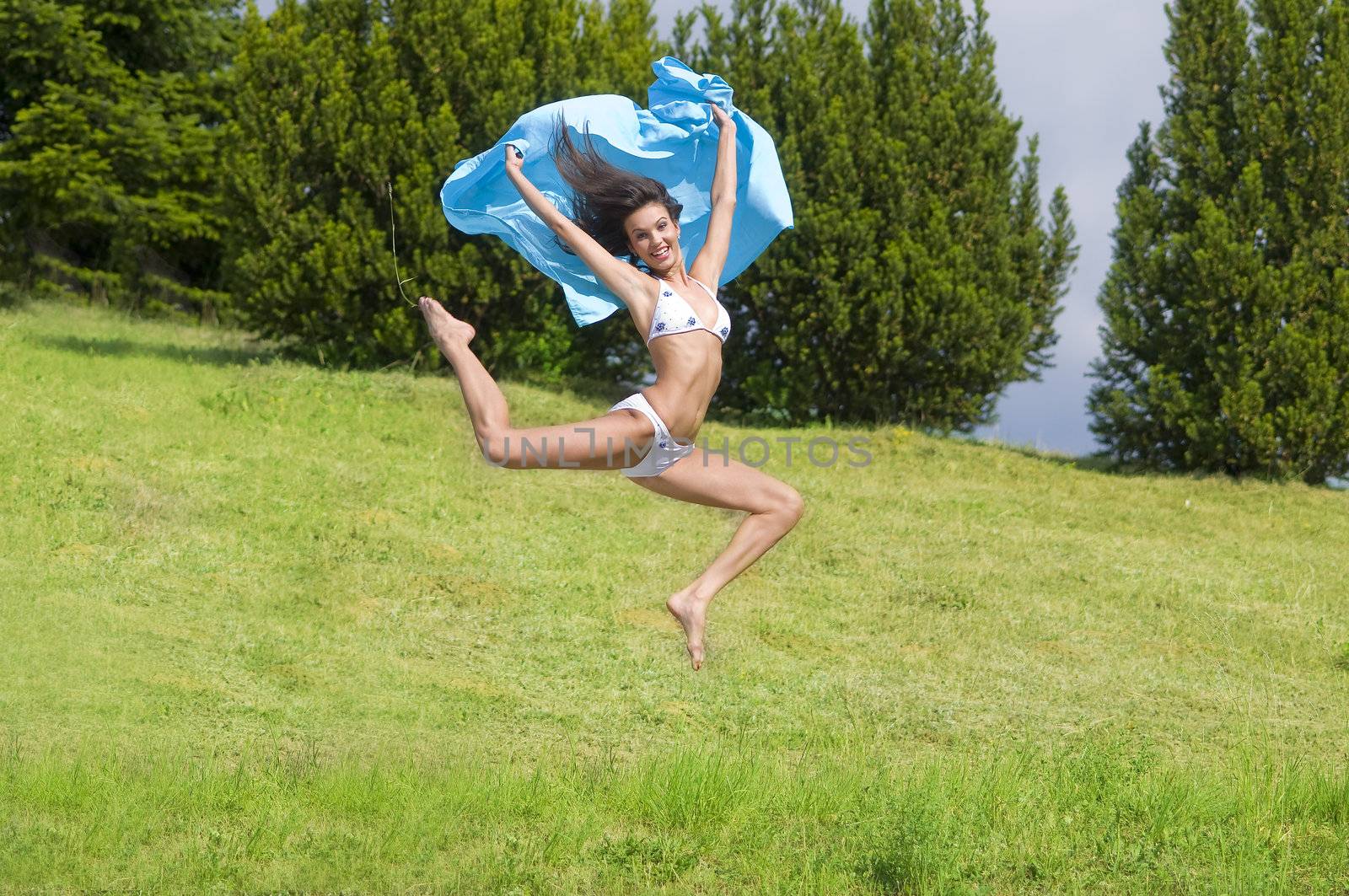 young woman jumping in a field with a blue scarf and white bikini