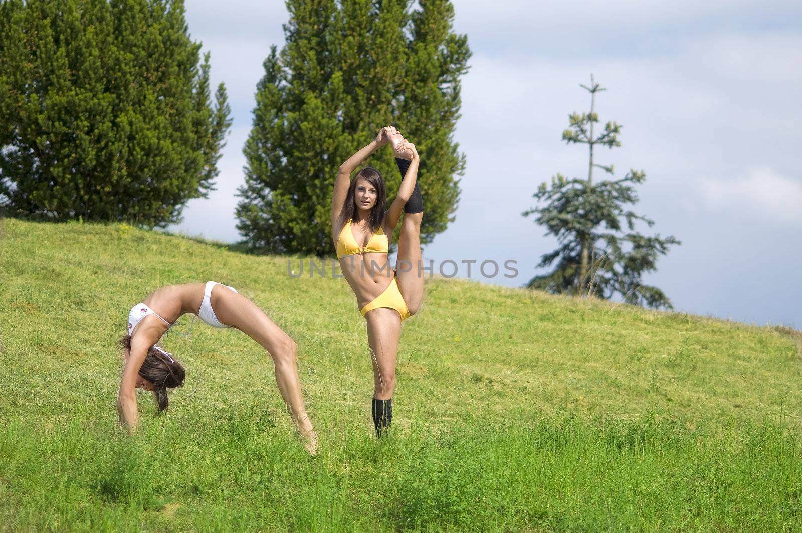 two girls jumping and stretching their body in a field
