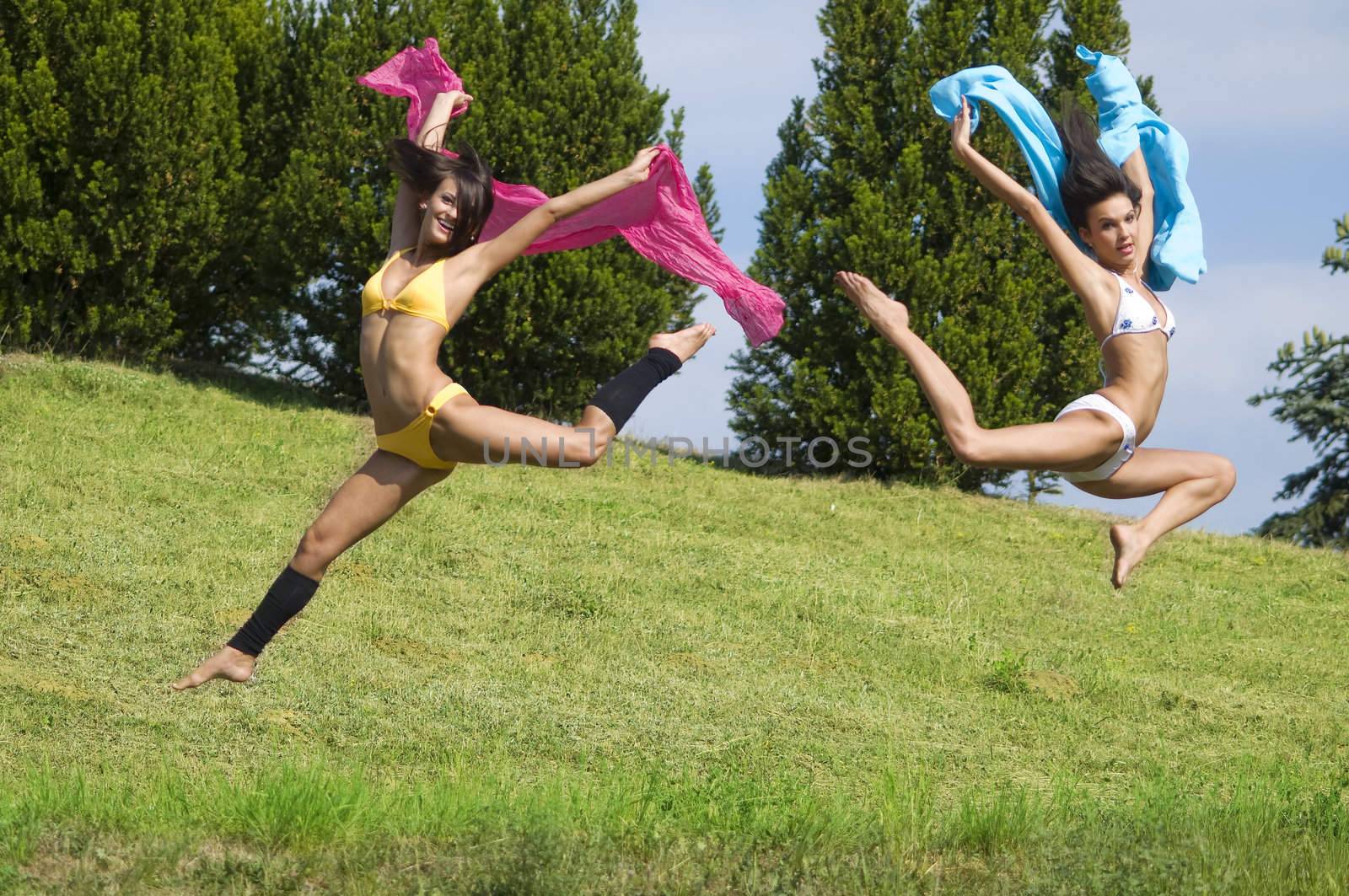 two great girls jumping tougheter in a field with pink and blue scarfe