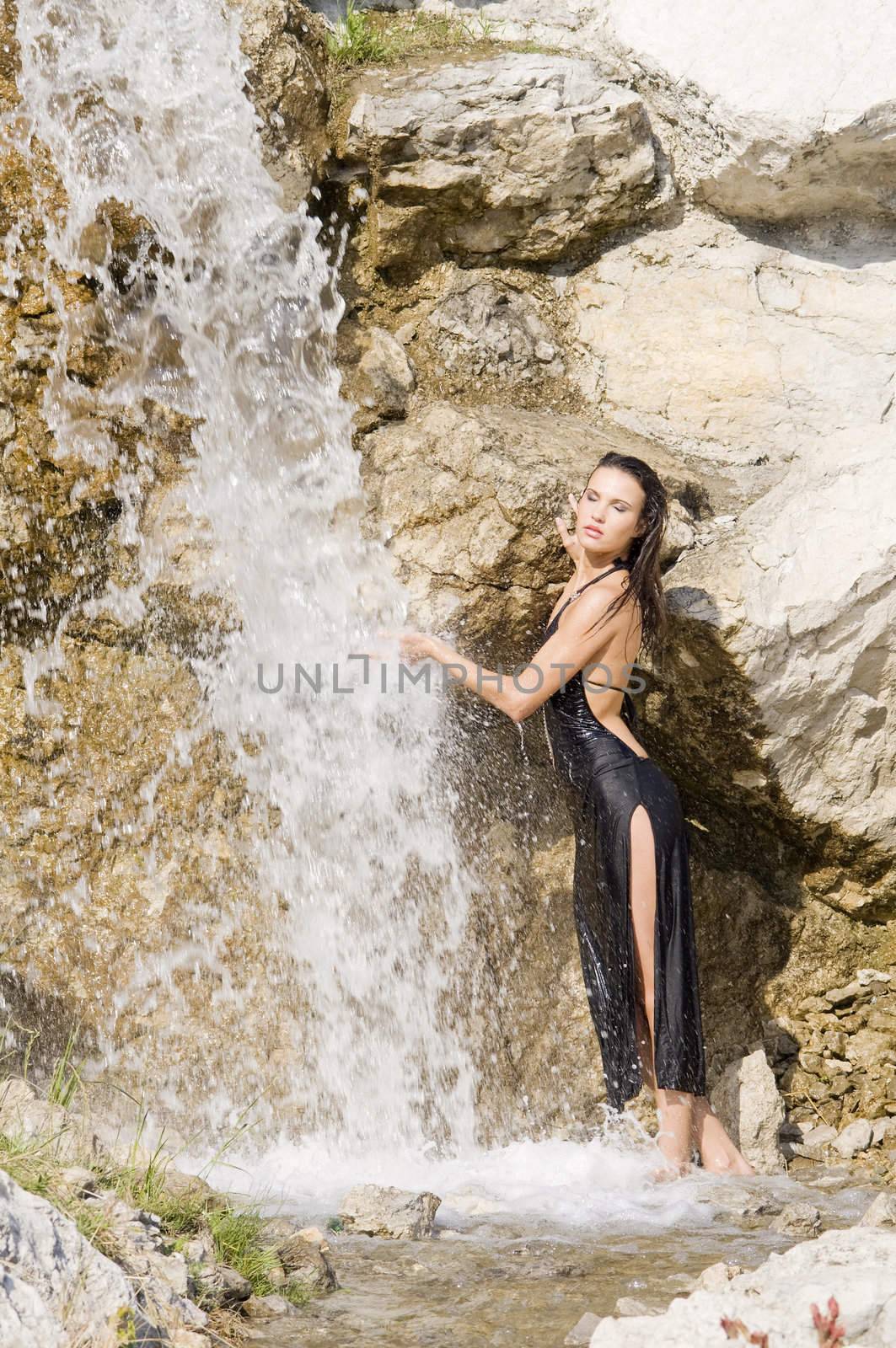 sexy brunette in black elegant dress taking shower in a waterfall