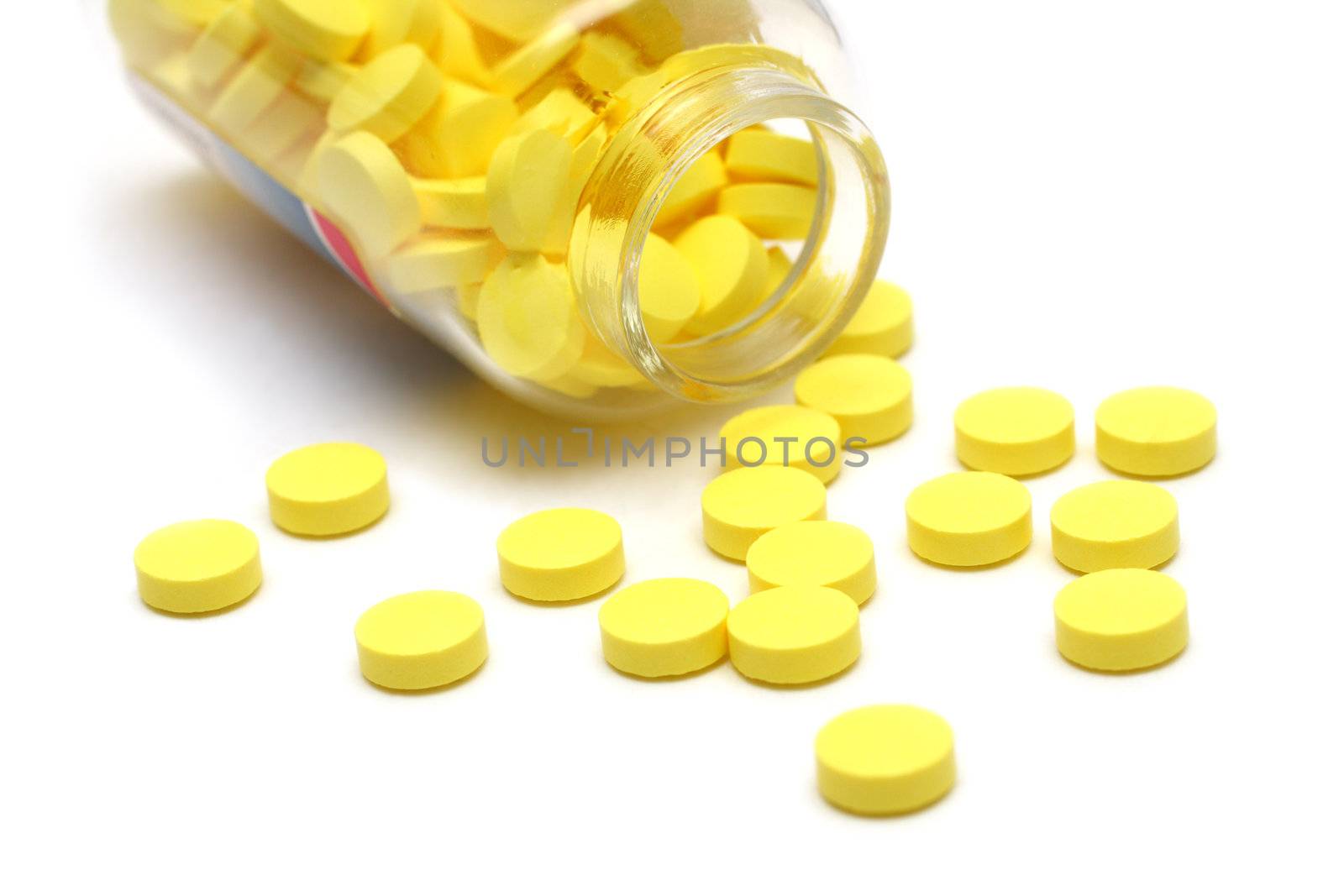 yellow pills around transparent bottle on white background