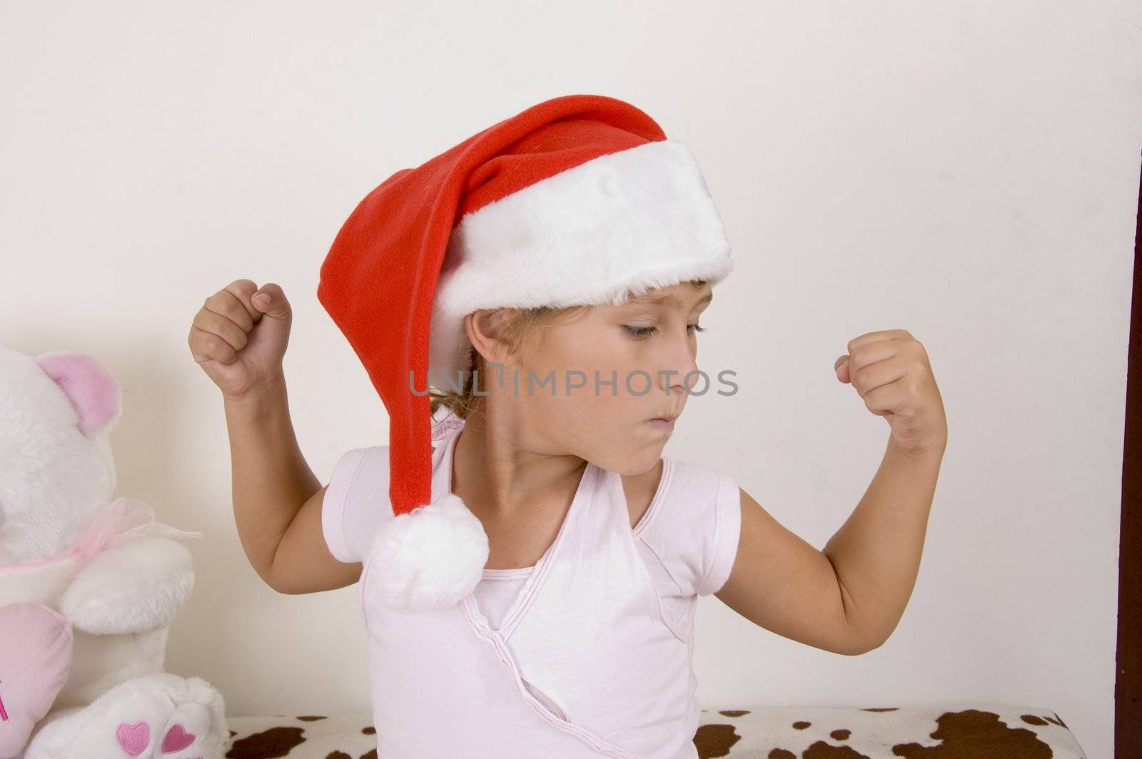 little girl wearing christmas hat and showing her muscles by imagerymajestic