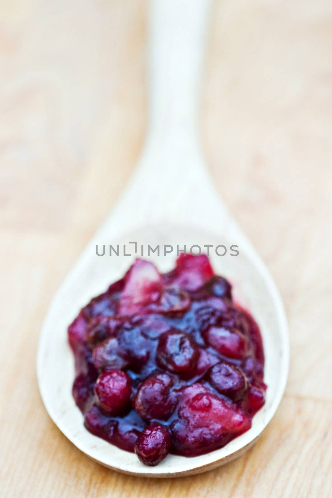 Large wooden spoon filled with homemade cranberry relish made with whole cranberries, raisins and apples. 