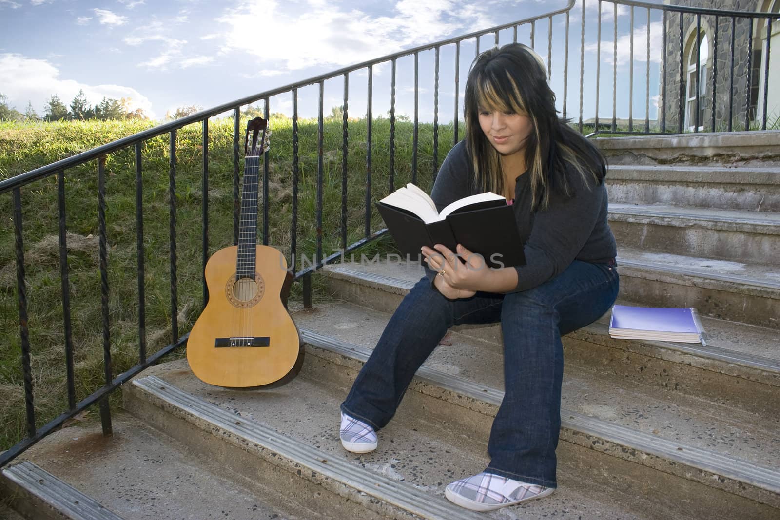 A young woman with highlighted hair reading a book or doing homework on campus.