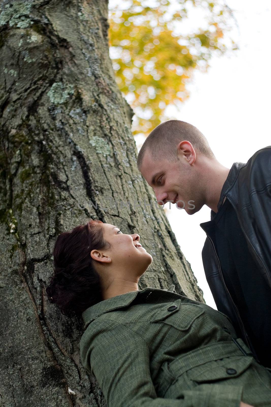 A young happy couple together outdoors by a tree on a fall day.