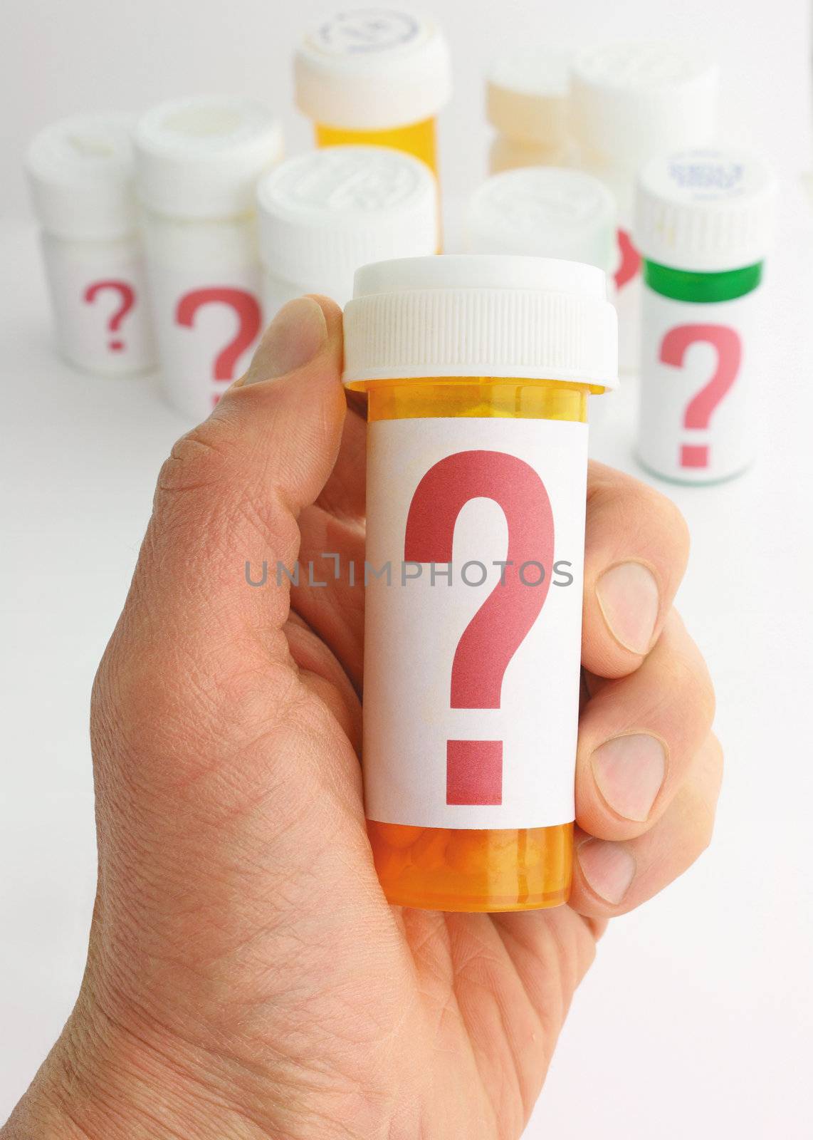closeup of a hand holding a medicine bottle marked with a large question mark. In the background is a group of pill bottles all labeled with large question marks. Image uses a somewhat shallow depth of field and background is moderately out of focus.