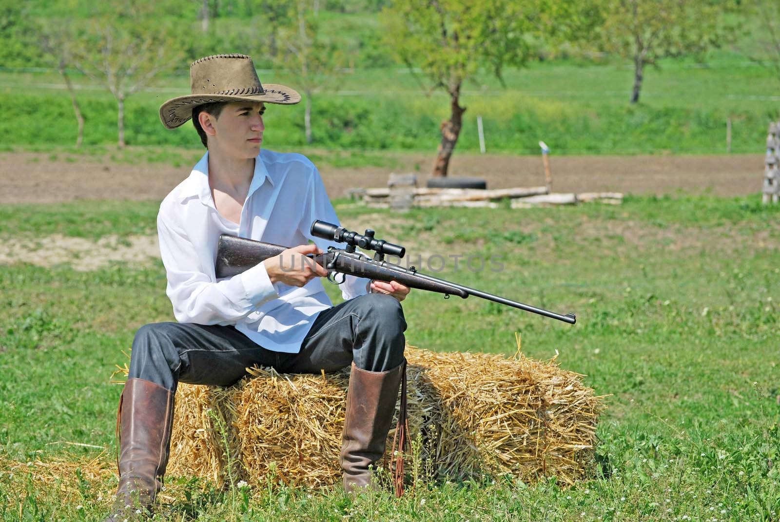 young cowboy holding a gun sitting on a hay bale