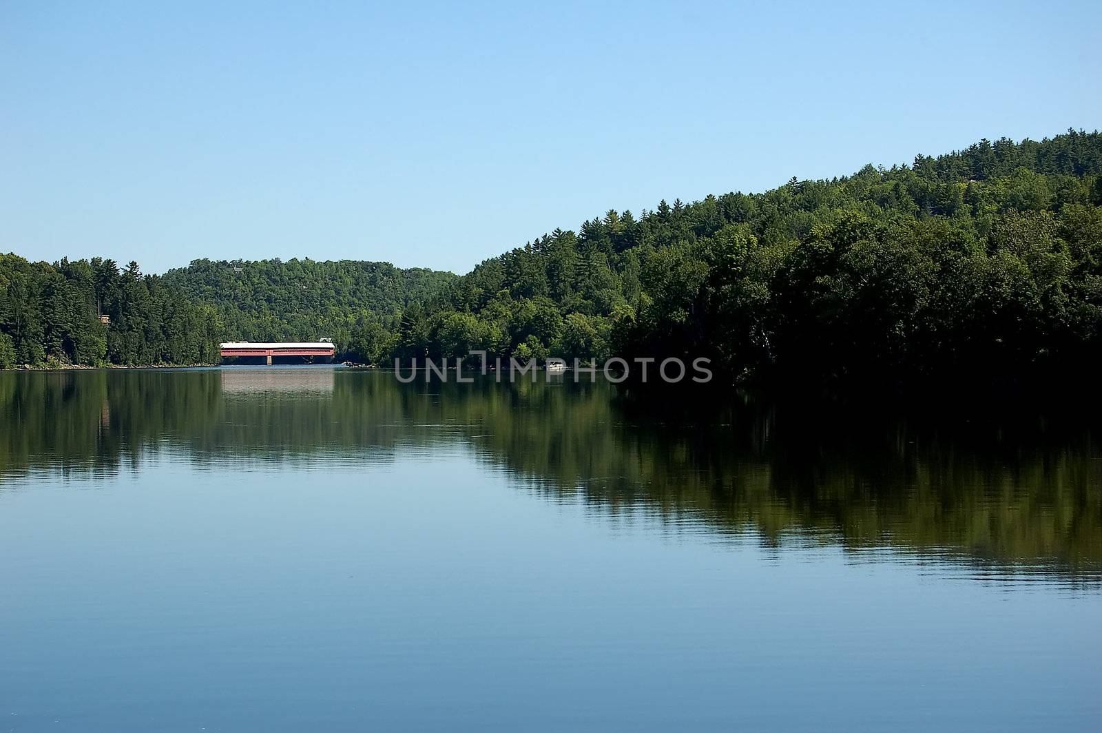 A calm river with a covered bridge in the distance