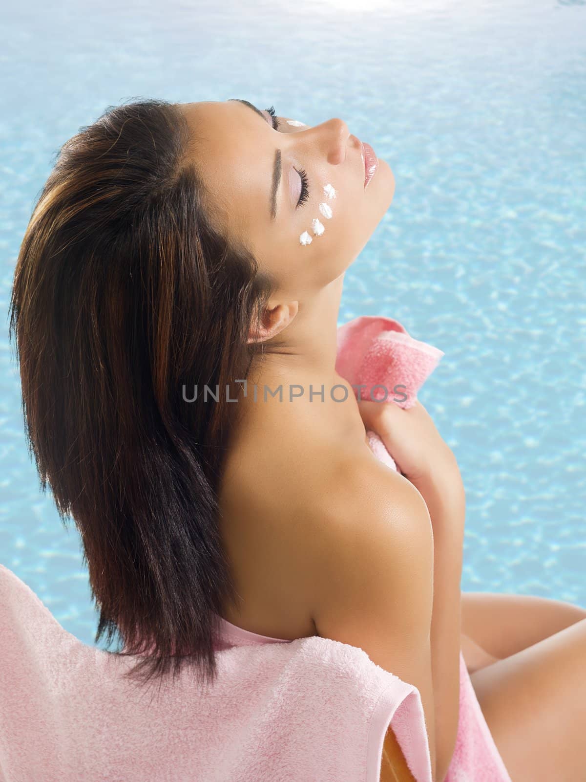 nice brunette wearing a pink towel with cream on face near a swimming pool