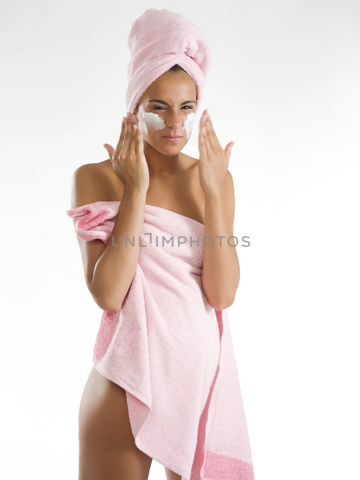 young and pretty girl with pink towel spreading on cream and making face